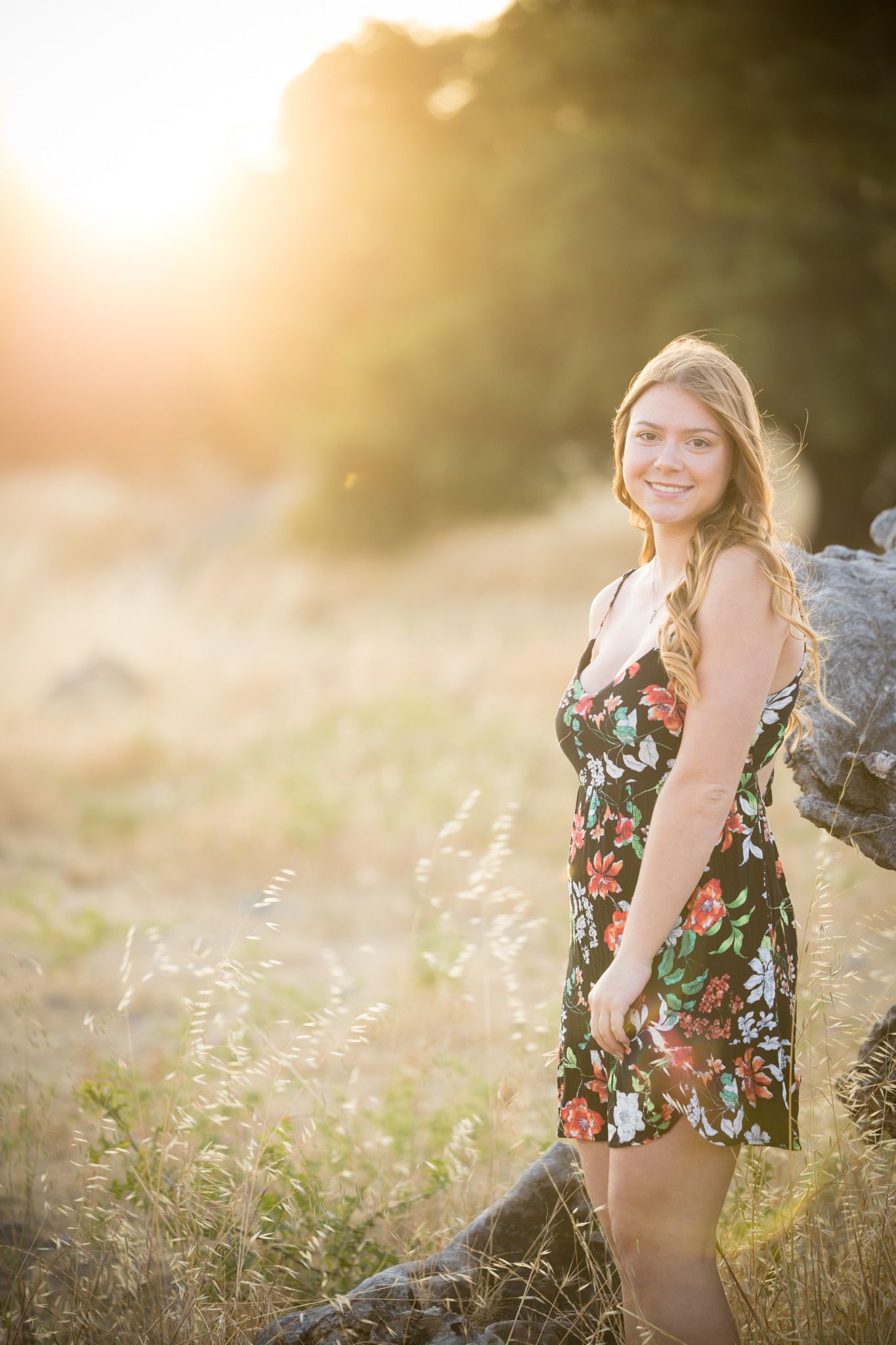 Golden hour portrait in floral dress against natural landscape.