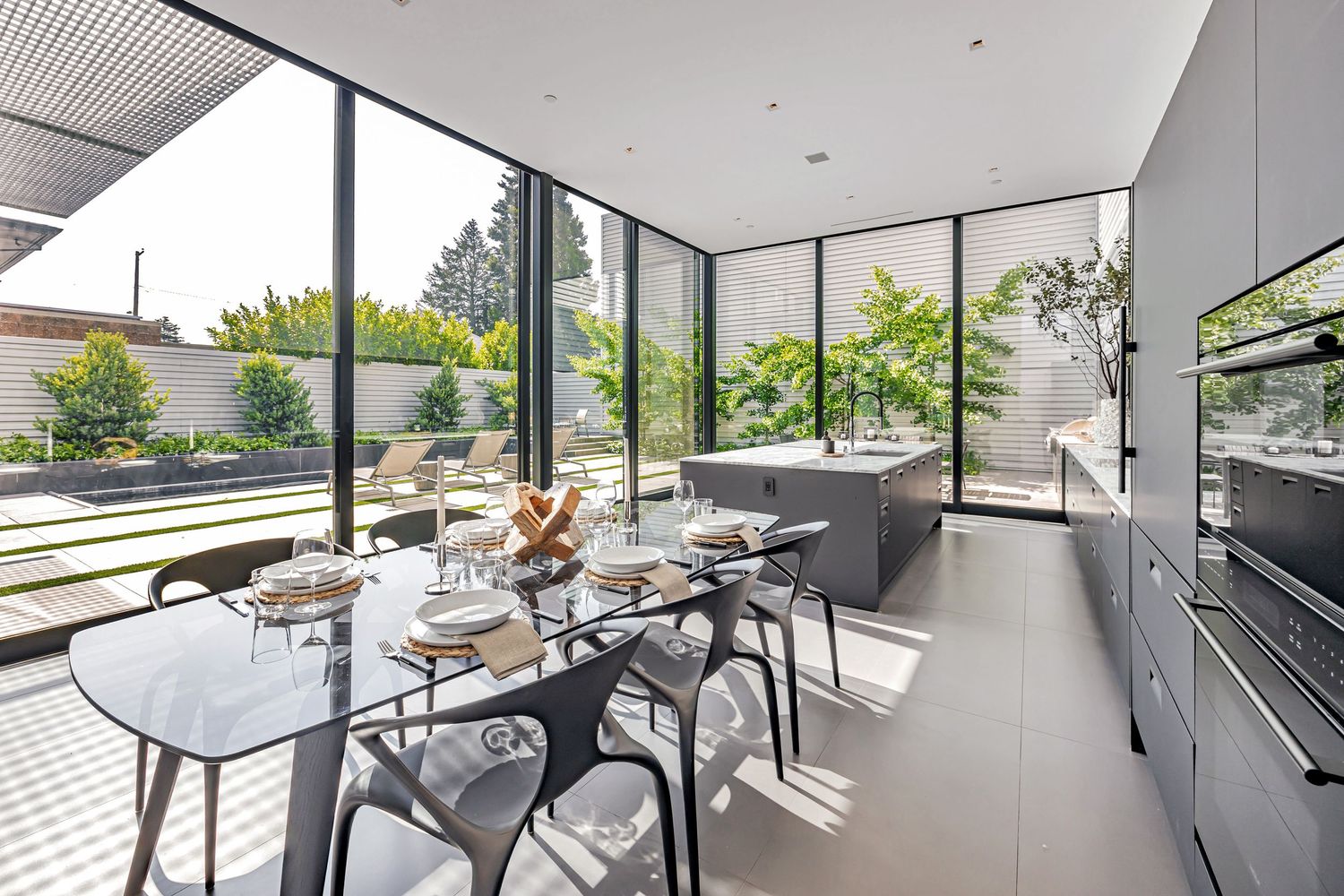 Contemporary minimalist dining area with glass walls and natural light illuminating the sleek interior design.