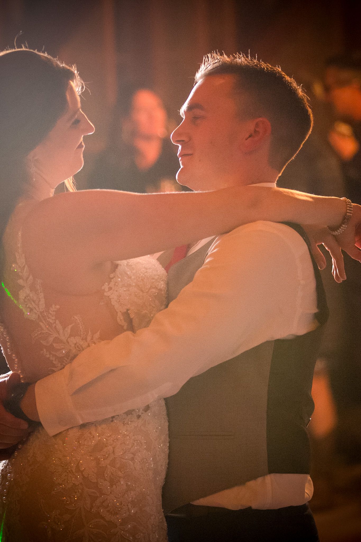 Romantic first dance between newlyweds with dramatic backlit lighting.