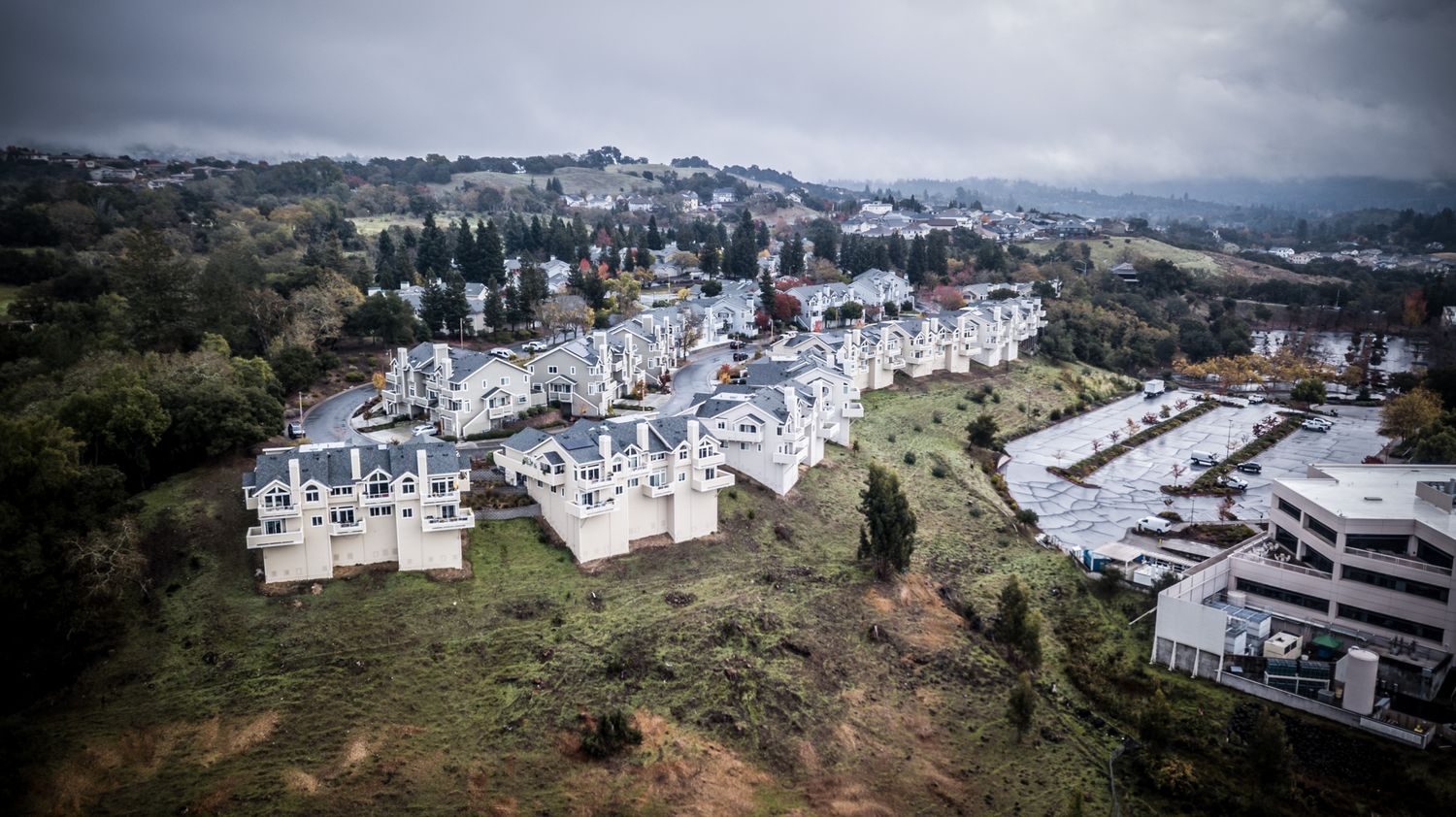 Aerial view of modern white hillside homes and buildings in a forested residential development.