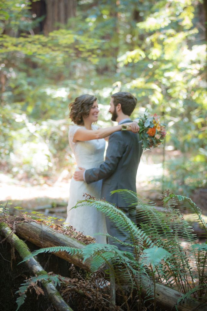 Tender moment between newlyweds surrounded by lush forest ferns and filtered sunlight.