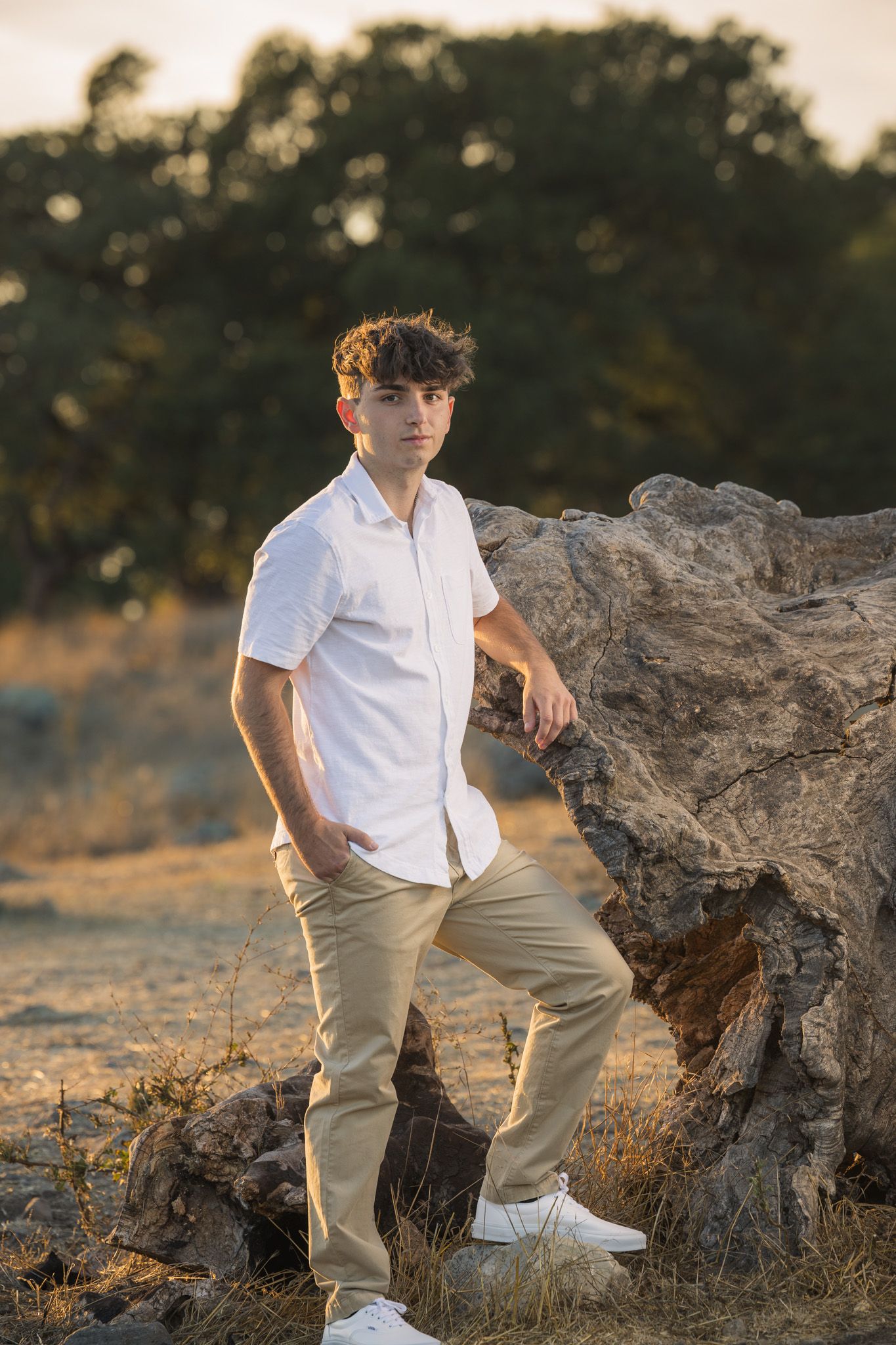 Casual outdoor portrait against weathered log in golden sunset light.