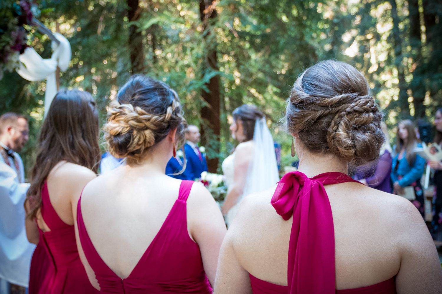 Bridesmaids in red dresses watching outdoor wedding ceremony from behind.