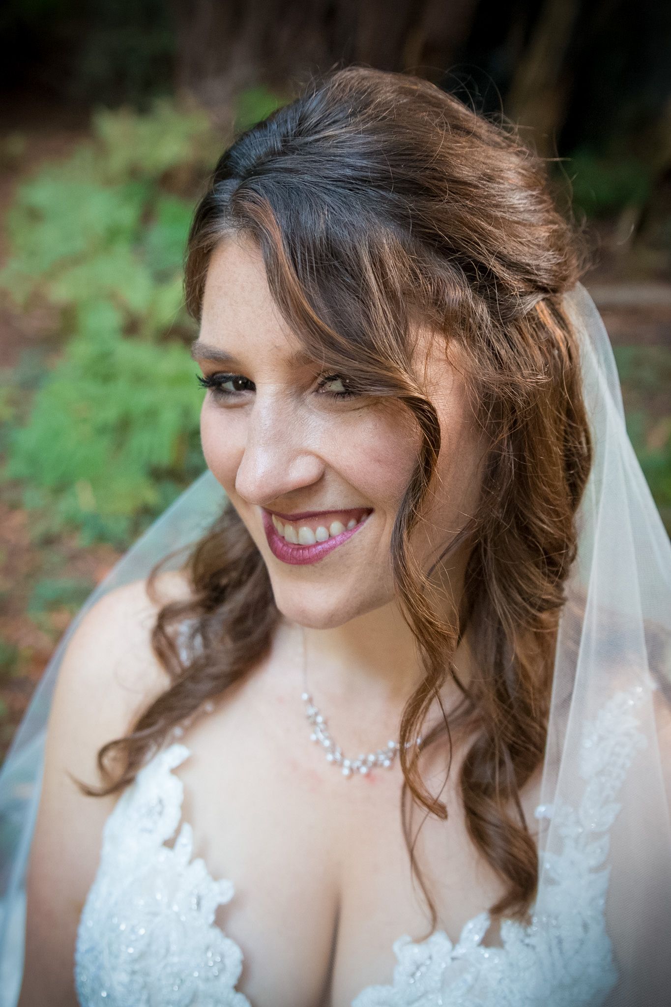 Close-up portrait of smiling bride wearing lace dress and crystal necklace.