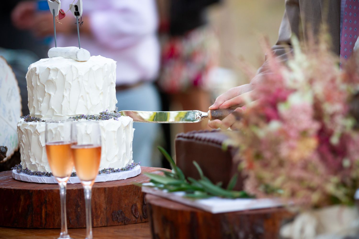 White wedding cake and champagne flutes displayed on wooden surface with pink floral decorations.
