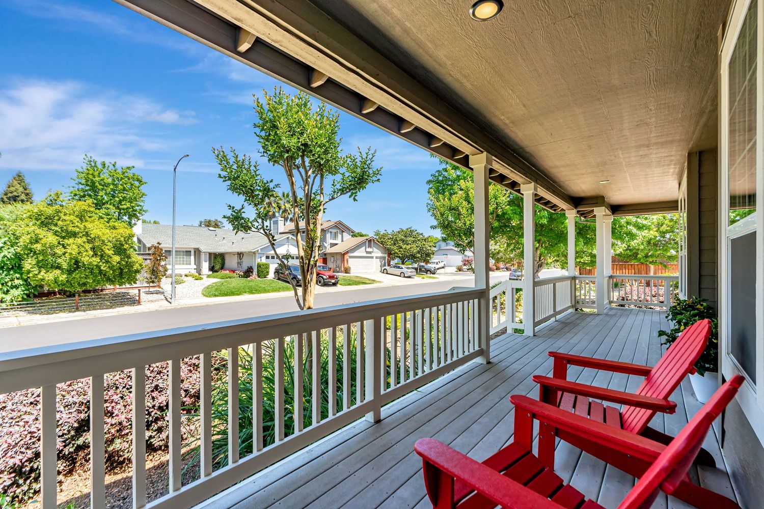 Covered porch with red Adirondack chairs overlooking neighborhood street view.