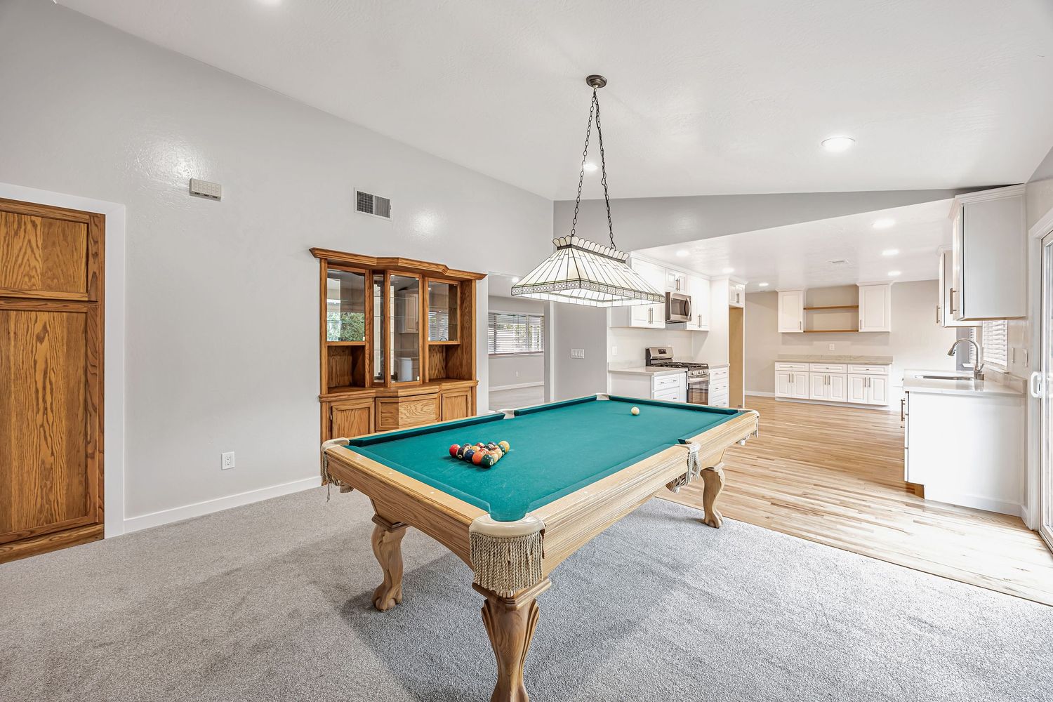Spacious entertainment area with pool table, wood hutch, and open kitchen view.