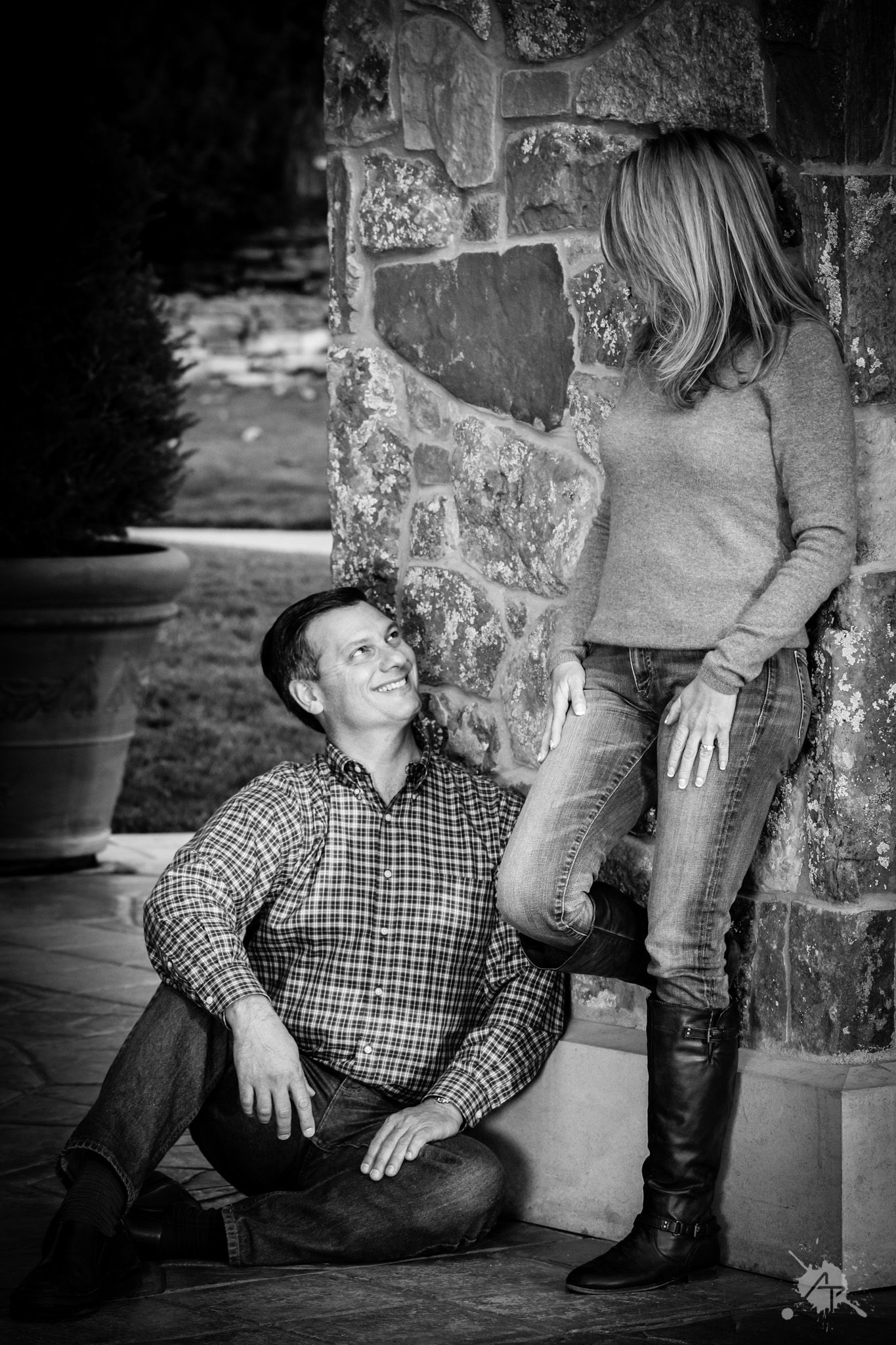Black and white engagement photo with rustic stone wall backdrop.