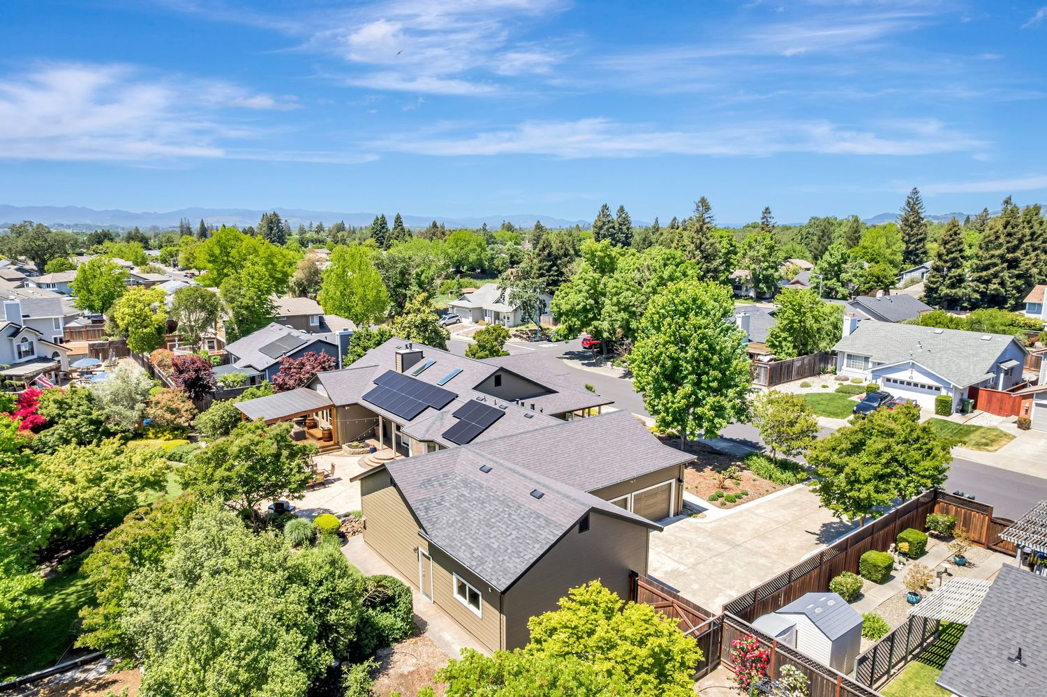 Birds-eye view of modern suburban homes with solar panels nestled among lush green trees.