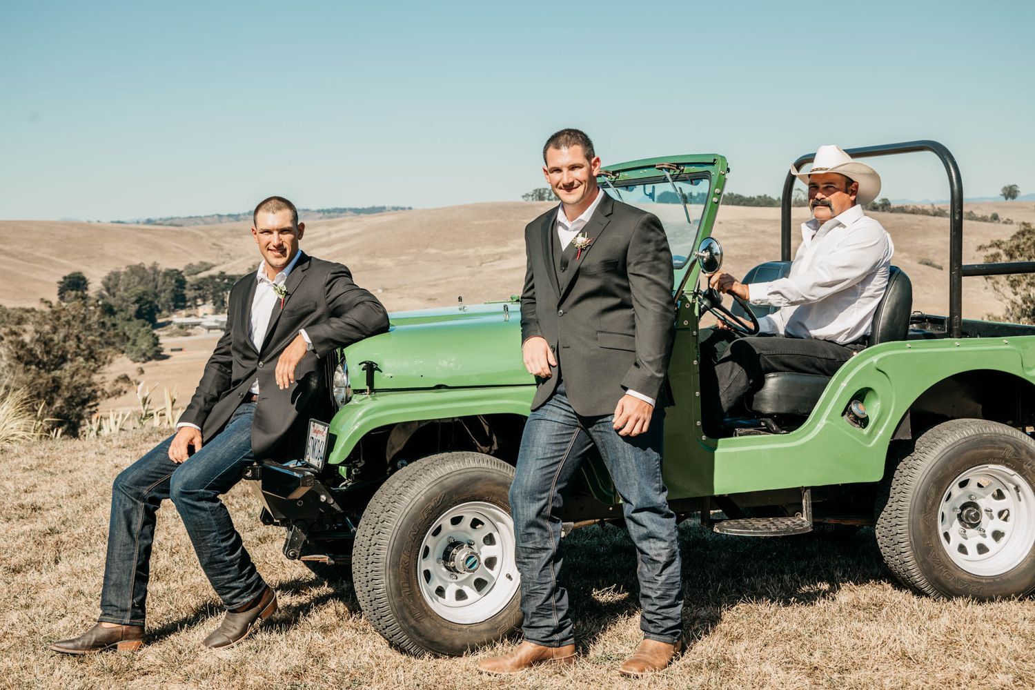 Three people pose with a green vintage-style Jeep in an open field.