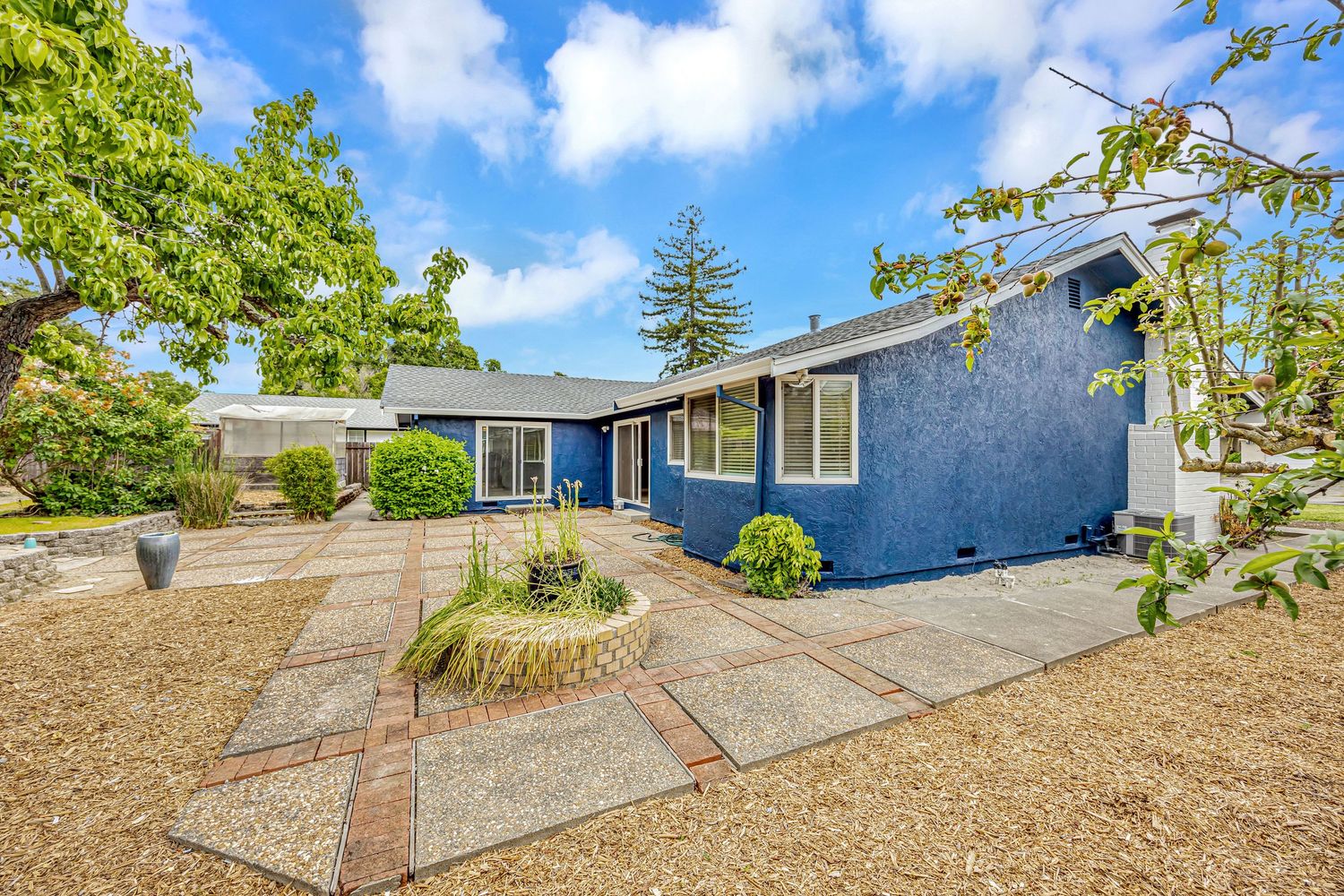 Modern blue ranch house with concrete walkway and drought-resistant landscaping under bright blue sky.