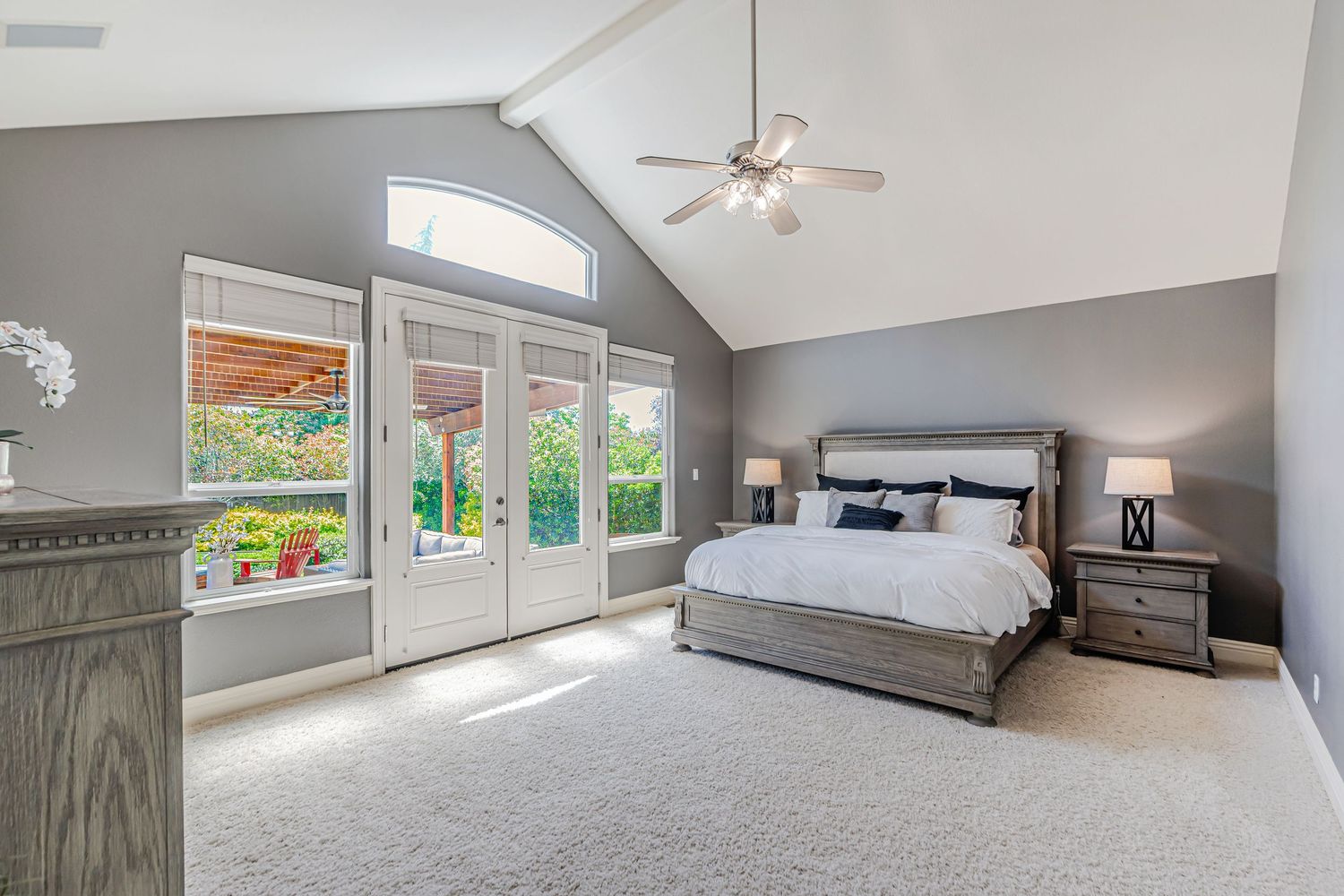Spacious master bedroom with vaulted ceiling, large windows, and plush carpet in contemporary gray tones.