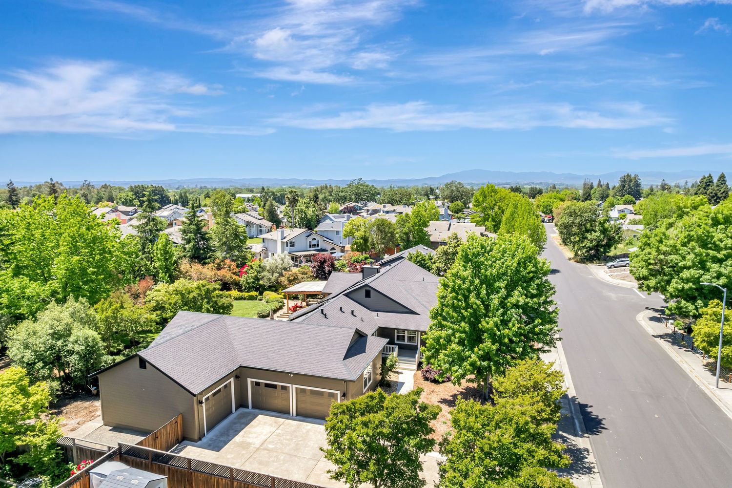 Bird's eye view of suburban homes with green trees and winding roads on a clear summer day.