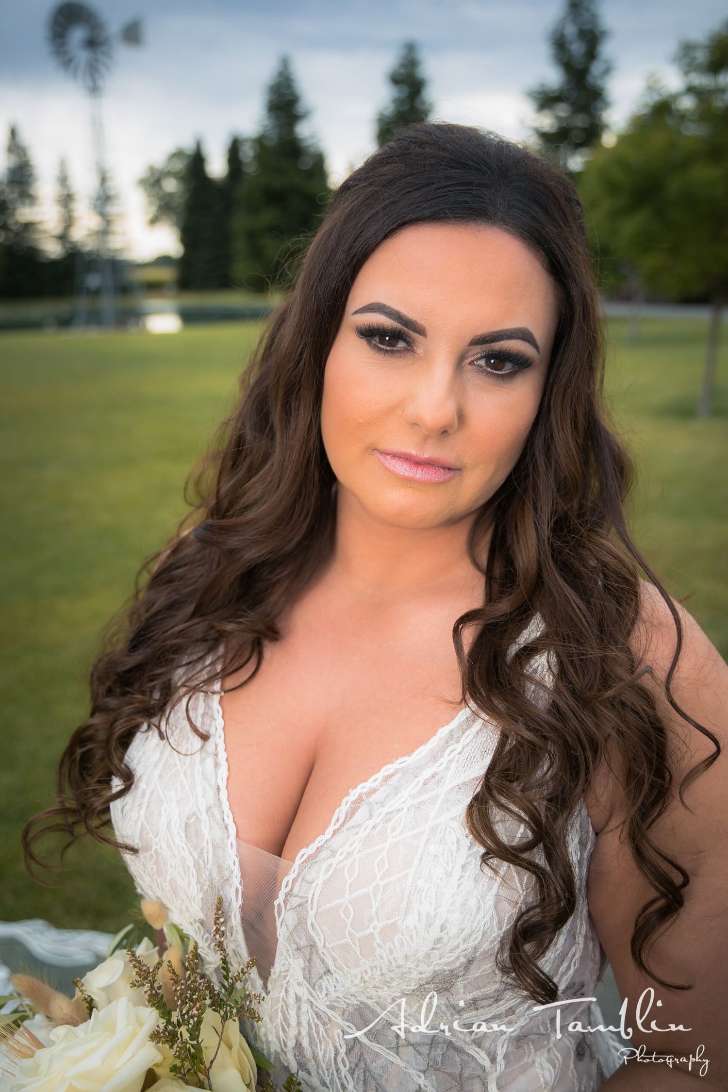 A bride in a white lace gown poses outdoors at dusk.