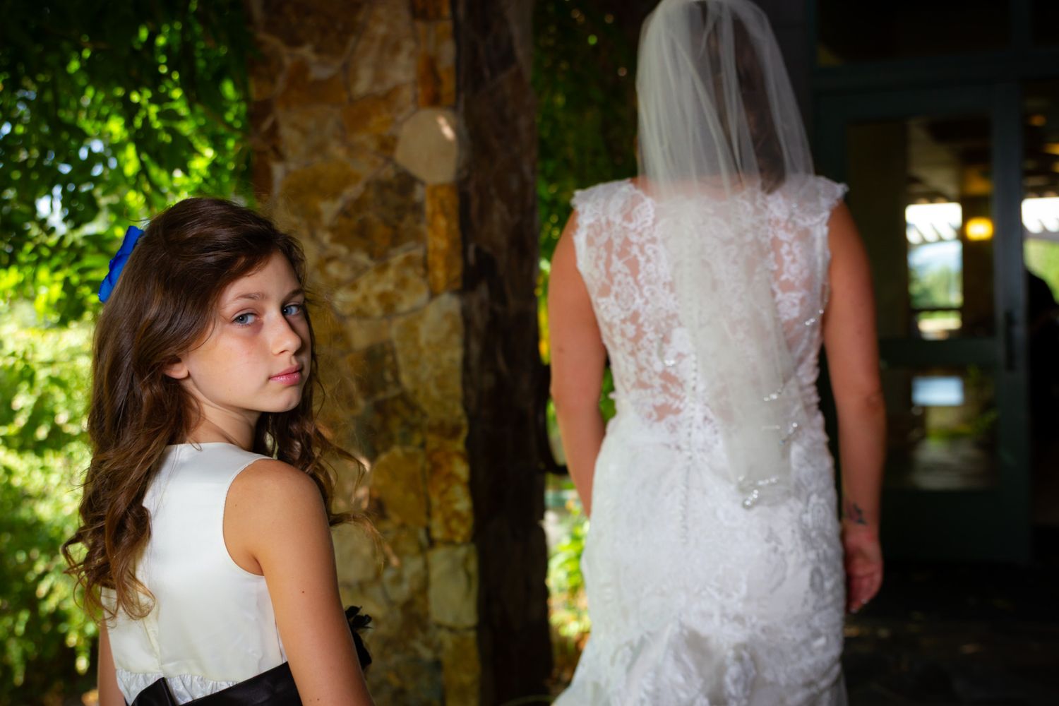 A young attendant watches as bride stands in lace wedding gown.