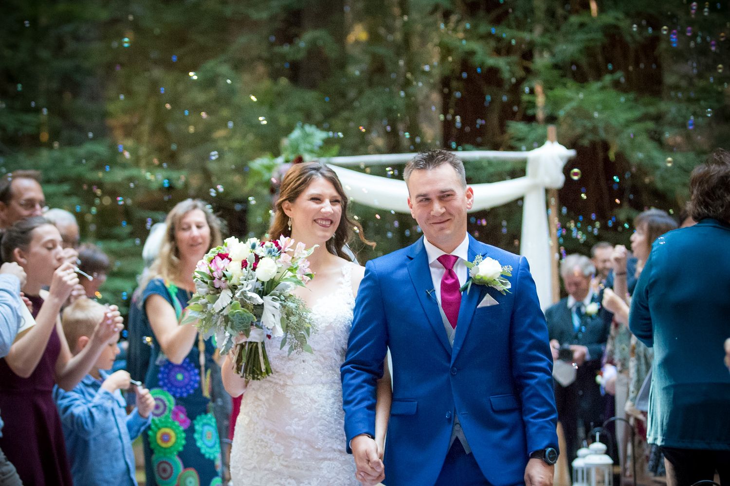 A wedding celebration in an outdoor forest setting with confetti being thrown over the newlyweds.