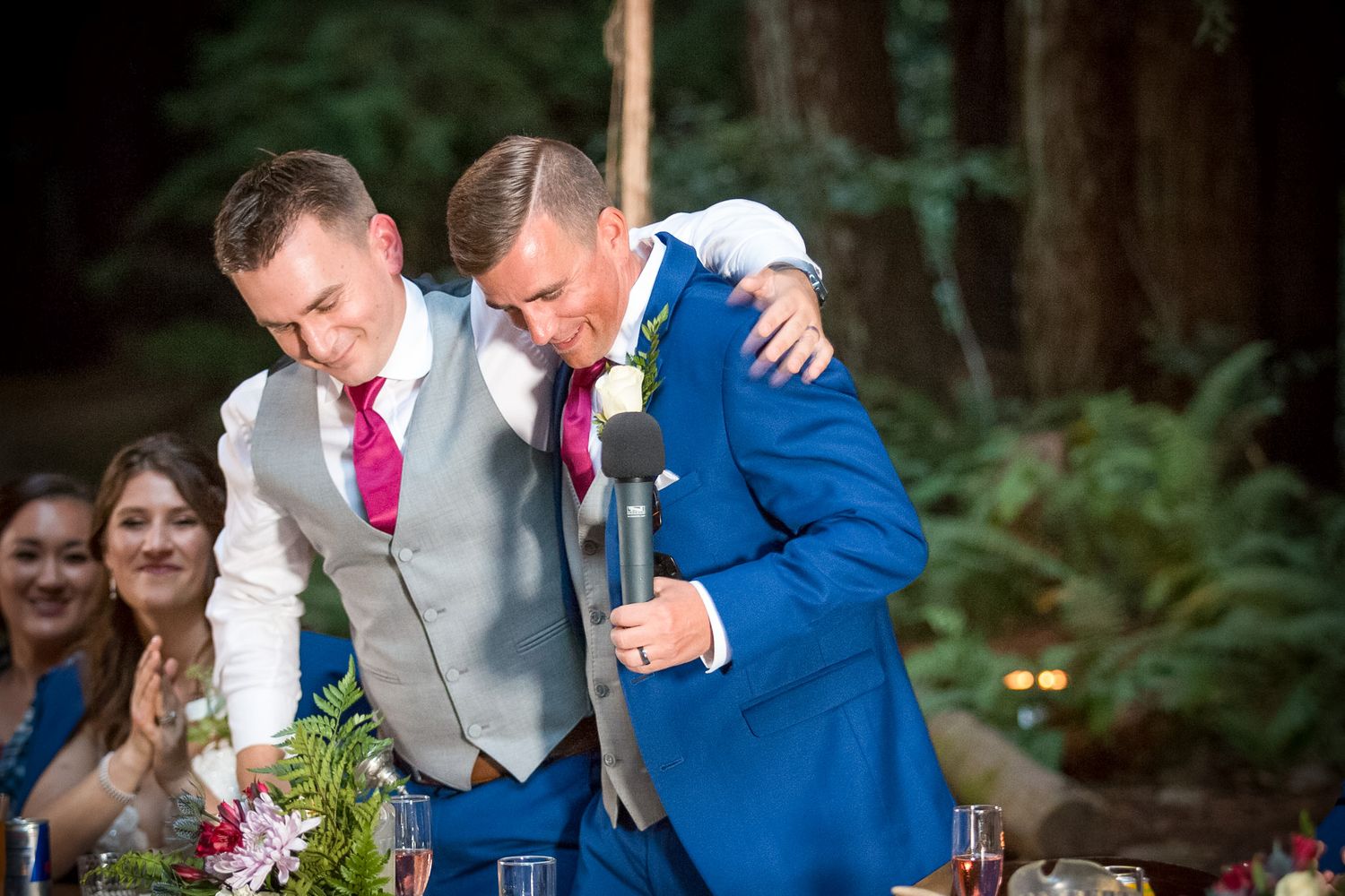 Two men in formal attire sharing an emotional moment at an outdoor wedding reception.