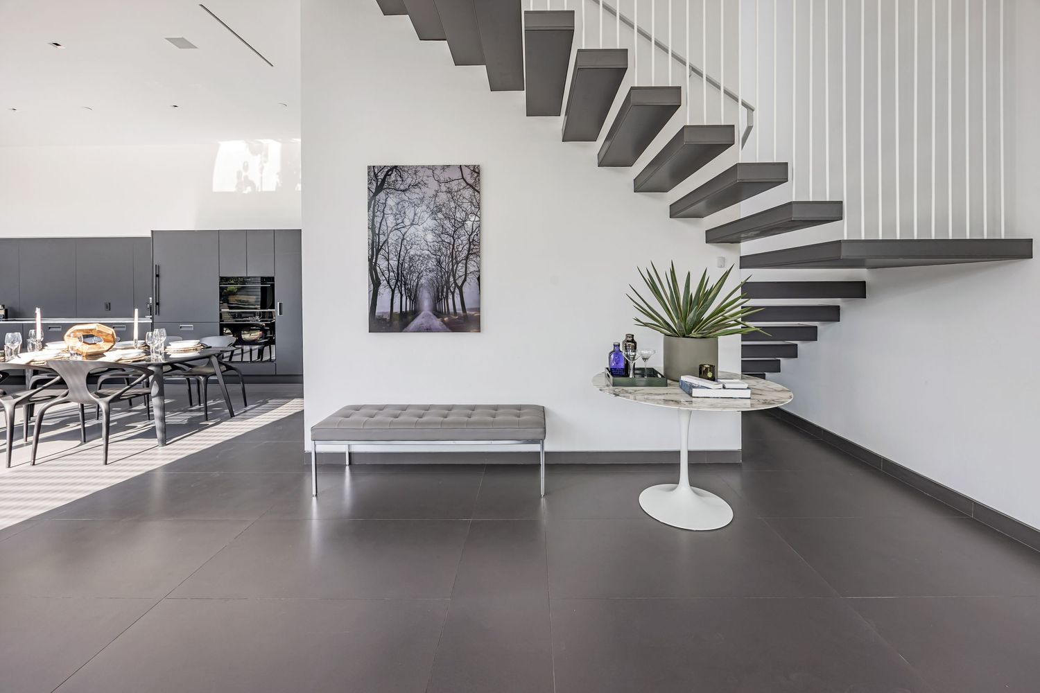Minimalist entryway featuring floating stairs, modern bench, and black and white tree artwork.