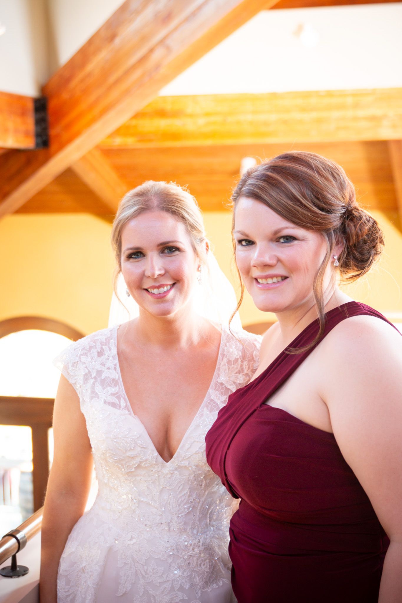 Bride in white lace dress poses with bridesmaid wearing burgundy dress.
