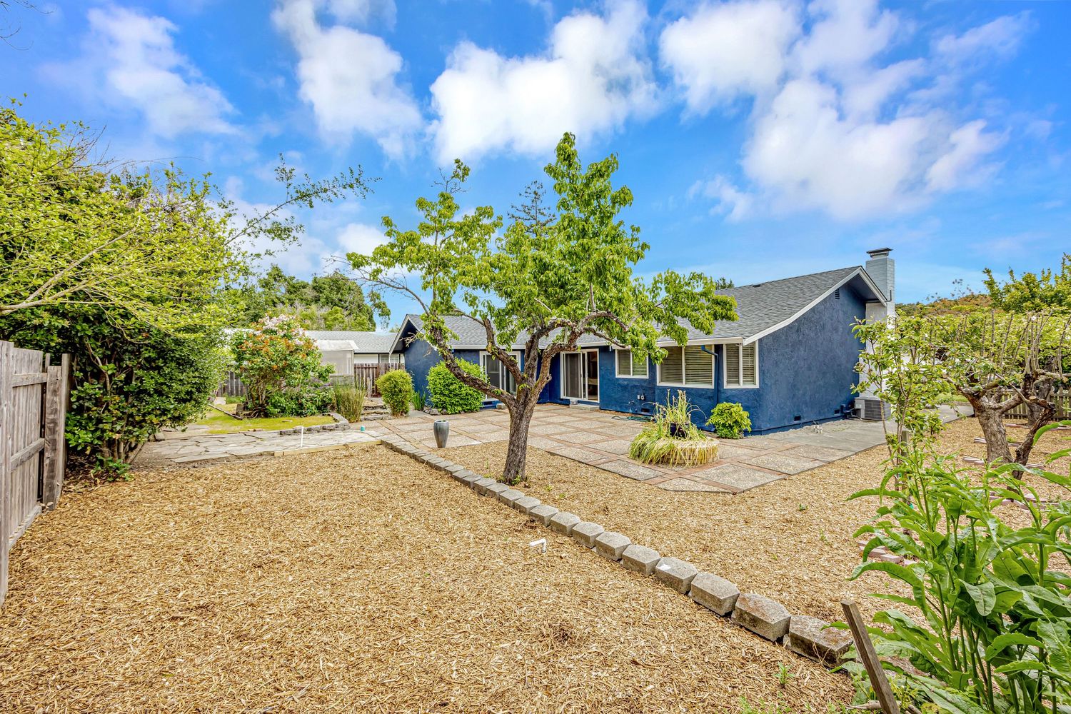 Side view of blue house with xeriscaped yard featuring trees and gravel ground cover.