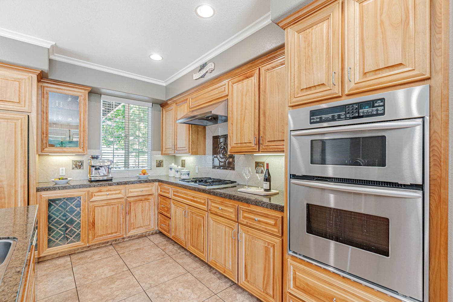Modern kitchen with light wood cabinets, stainless steel appliances, and granite countertops featuring a built-in double oven.