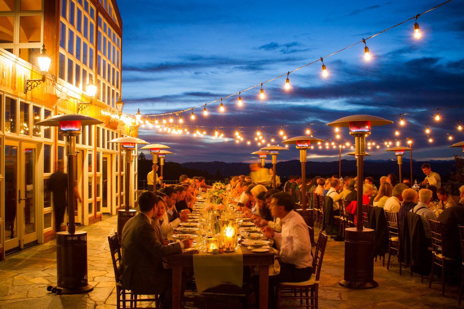 Evening outdoor wedding reception with string lights and long dining tables at dusk.