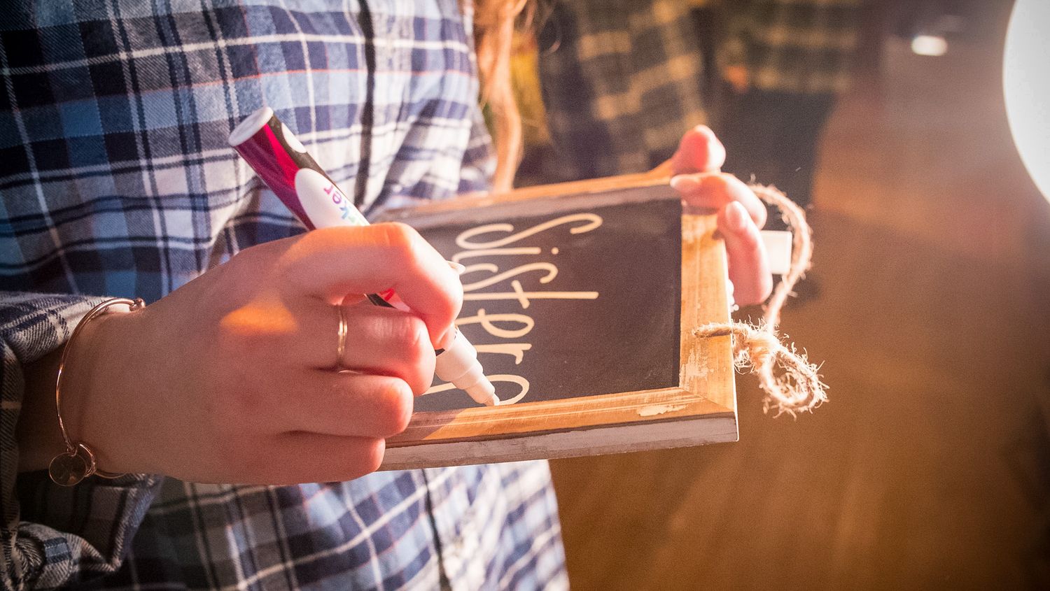 Hands holding a small wooden sign with writing on it in warm lighting.