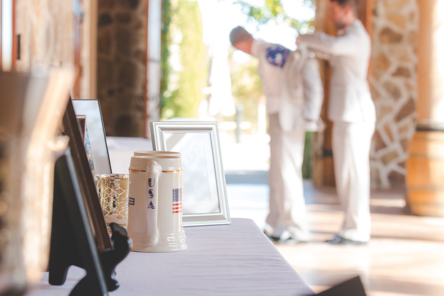 Picture frames and decor items line a table at a wedding venue with blurred figures in background.