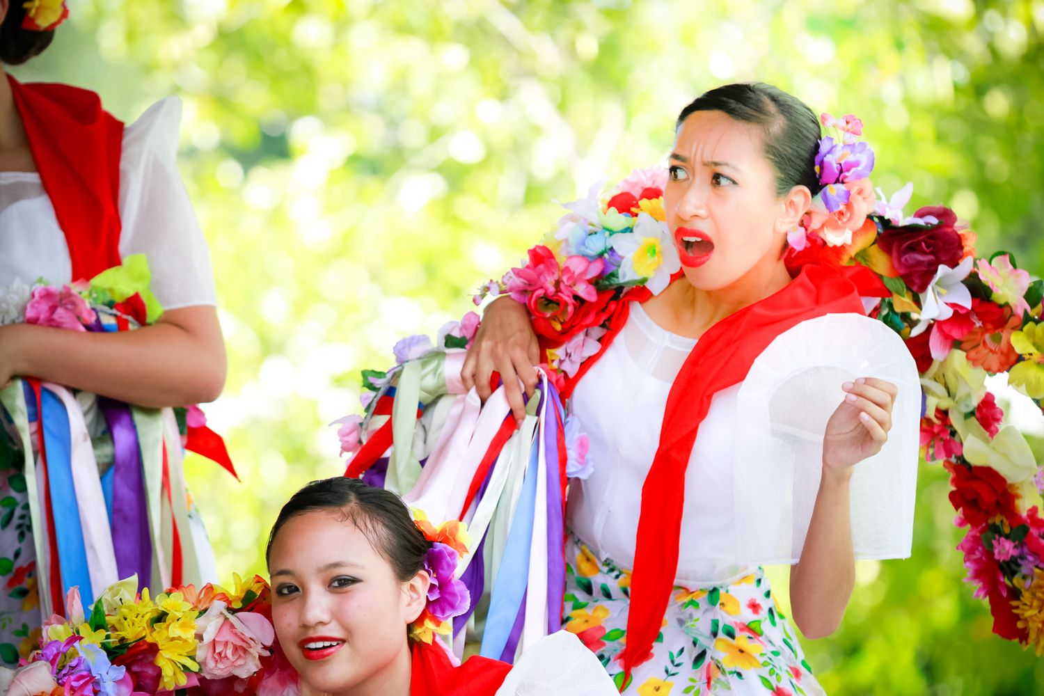 Performers wearing colorful Hawaiian leis and traditional costumes smiling during cultural celebration.