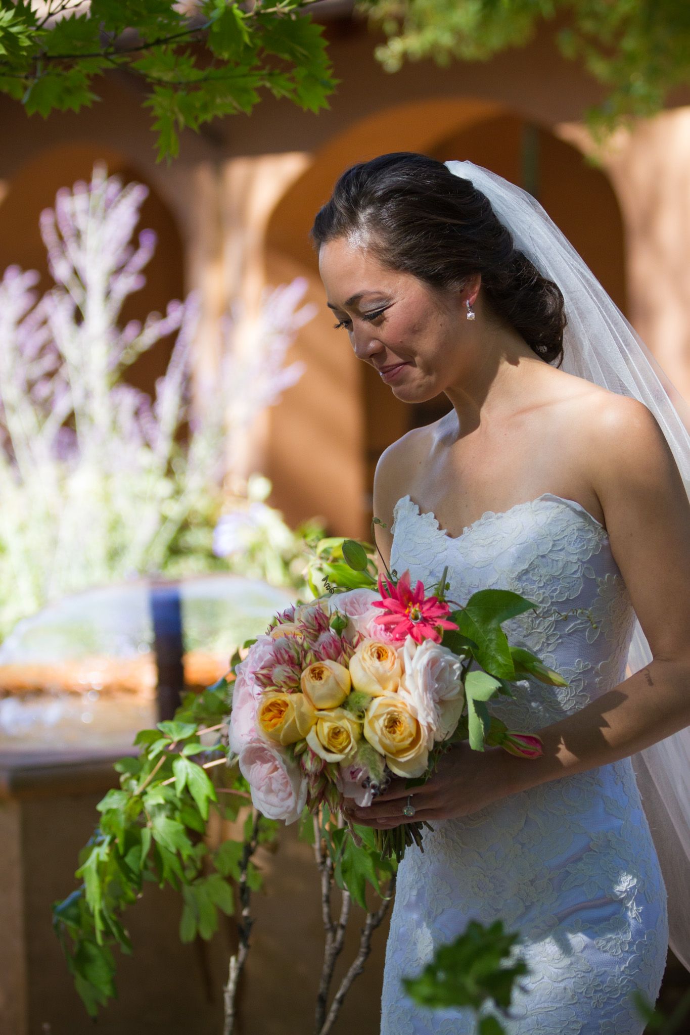 Wedding bouquet with pink and yellow roses held by someone in a white lace dress.