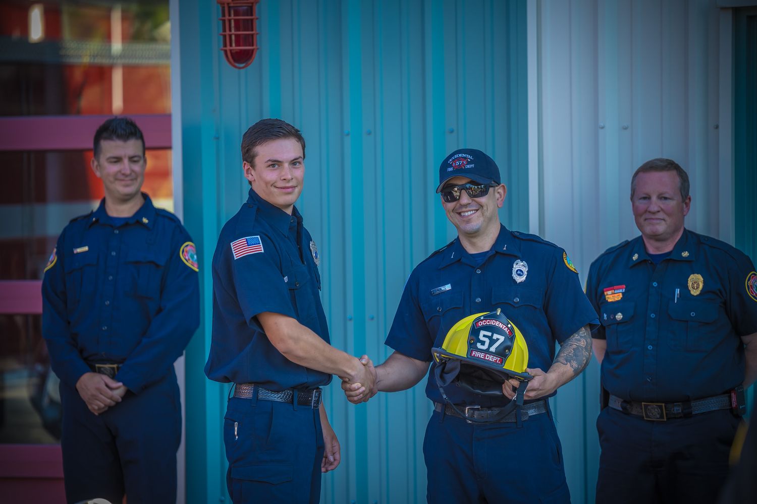 Public safety officers gather outside a blue building for a group photo.
