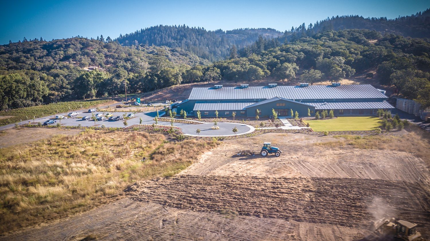 Aerial view of a modern winery facility nestled in rolling hills with parking area.