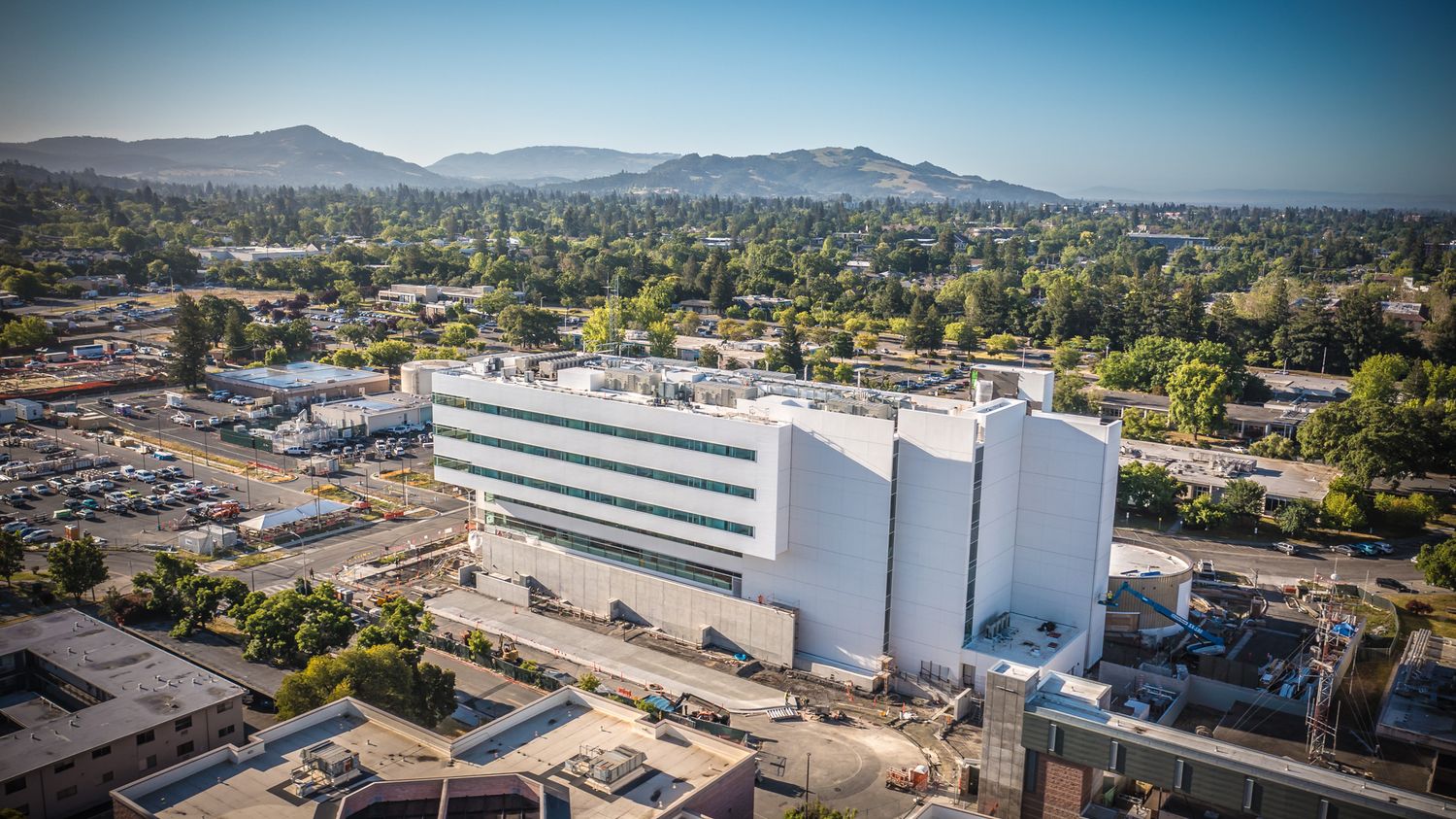 Modern industrial building with white silos against mountainous backdrop in suburban setting.