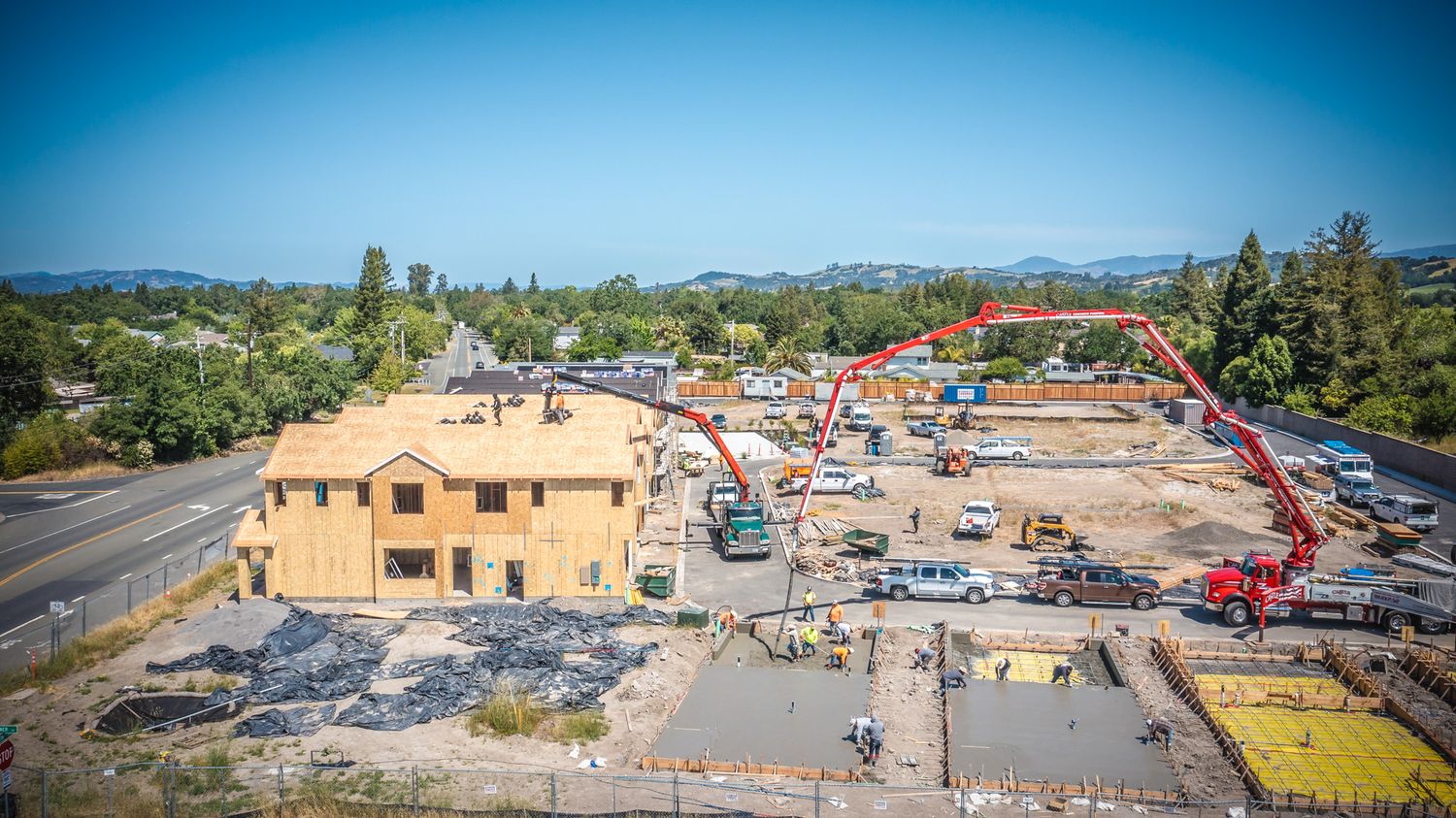 Construction site with concrete pumping trucks and workers building new residential structures.