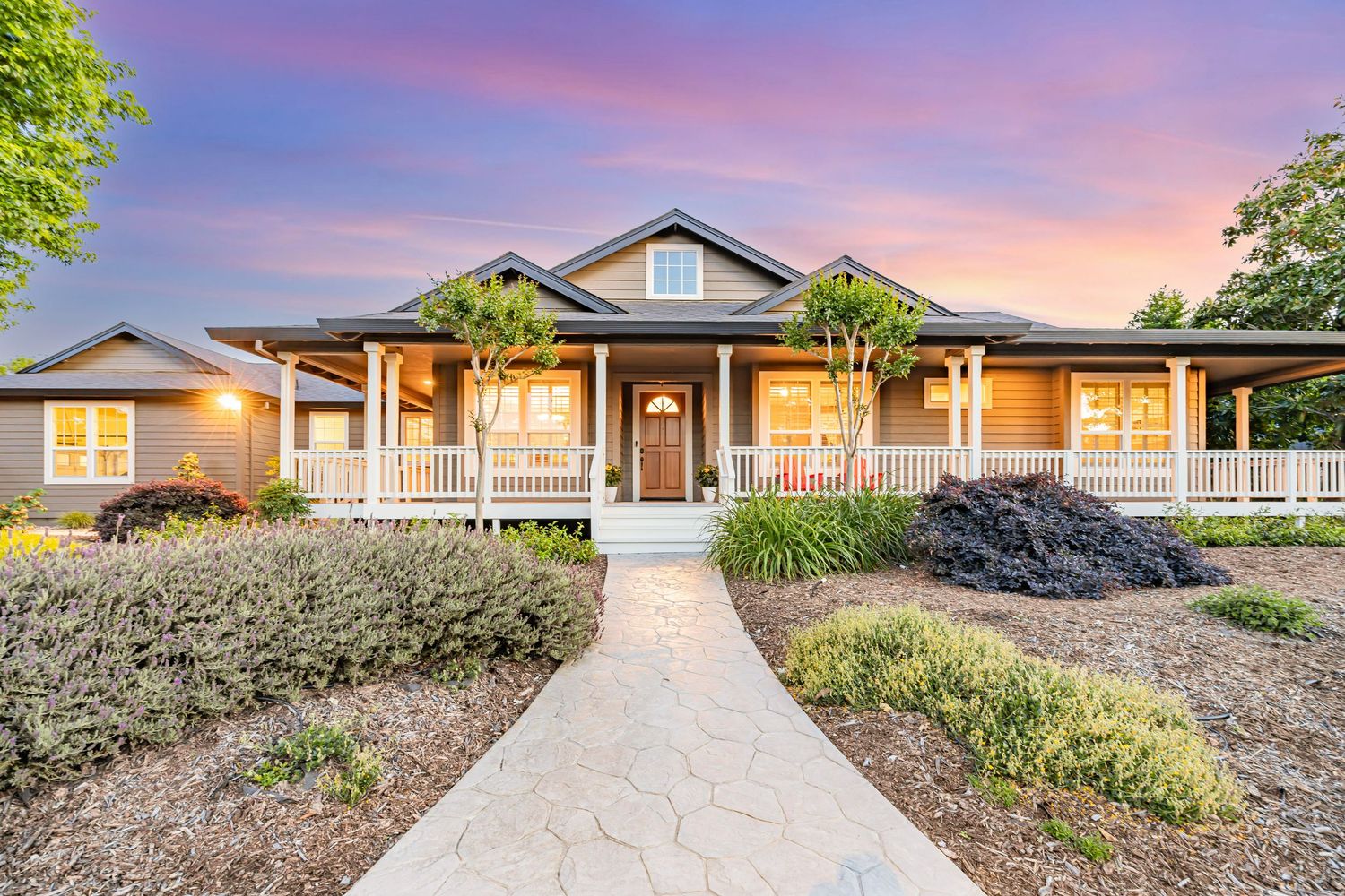 Elegant ranch style home with wrap-around porch and drought-resistant landscaping at twilight.