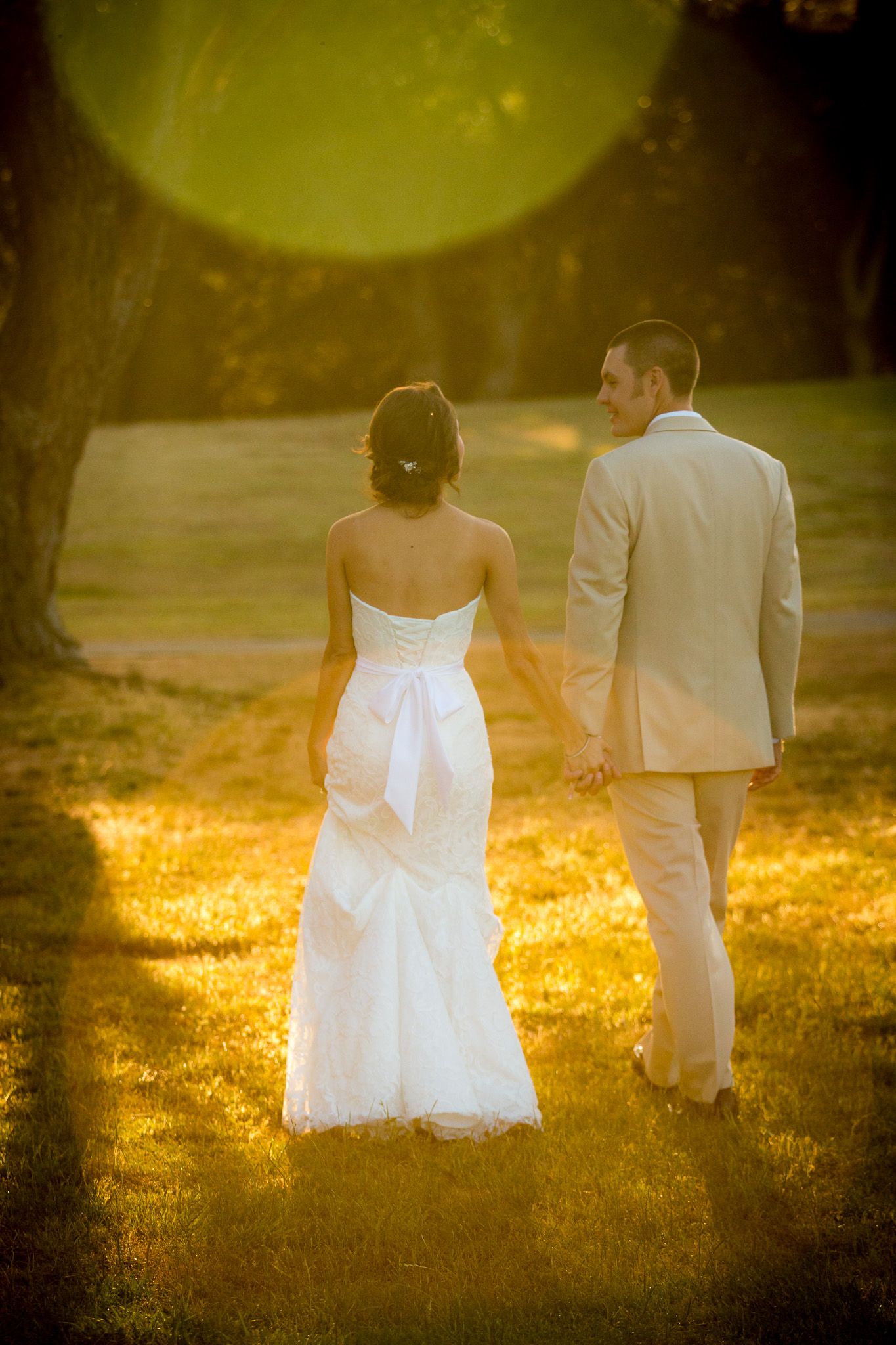 Newlywed couple holding hands in a golden sunlit garden with dreamy bokeh effect at sunset.