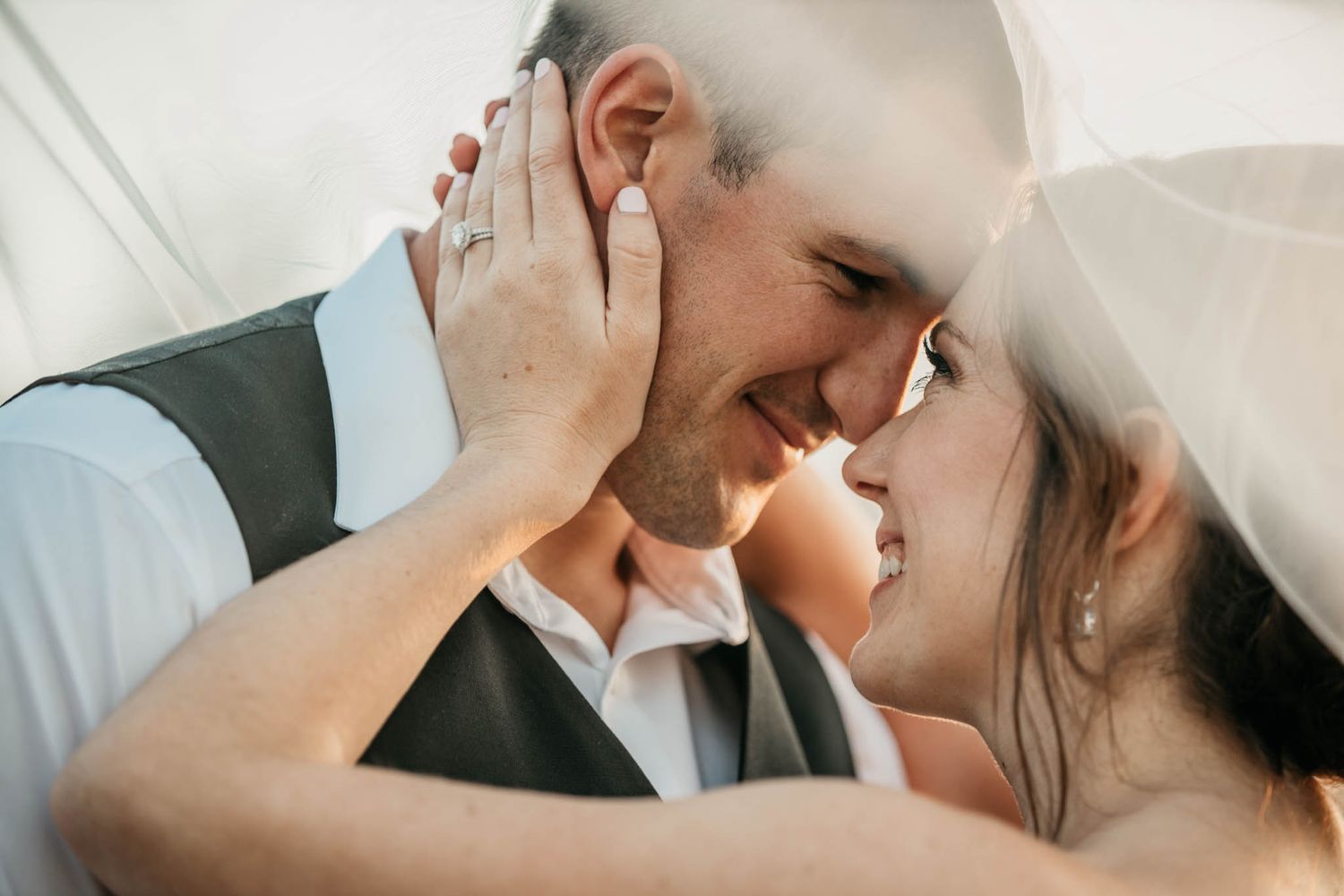 An intimate close-up moment between newlyweds sharing a tender moment under a veil.
