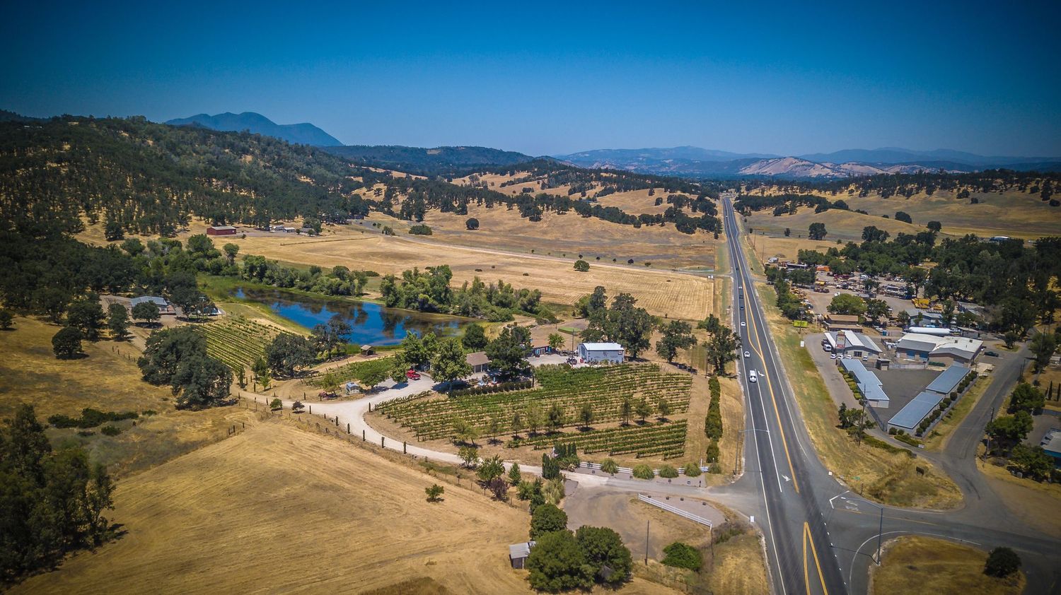 Aerial view of a rural highway cutting through golden hills with a blue lake visible.