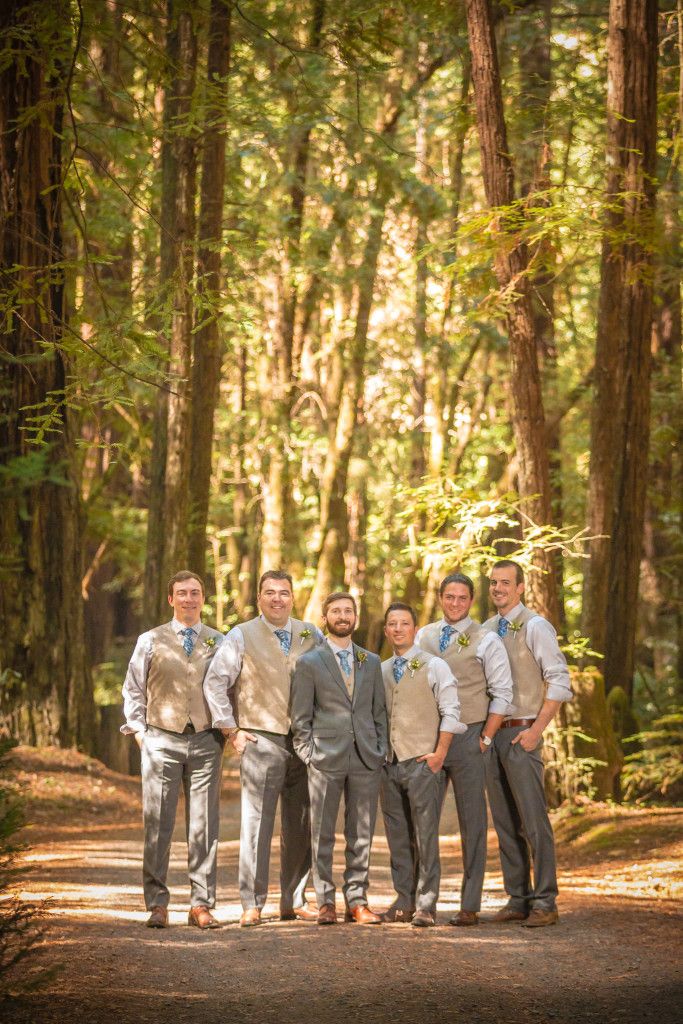 Wedding party in grey and tan suits standing together on a woodland trail.