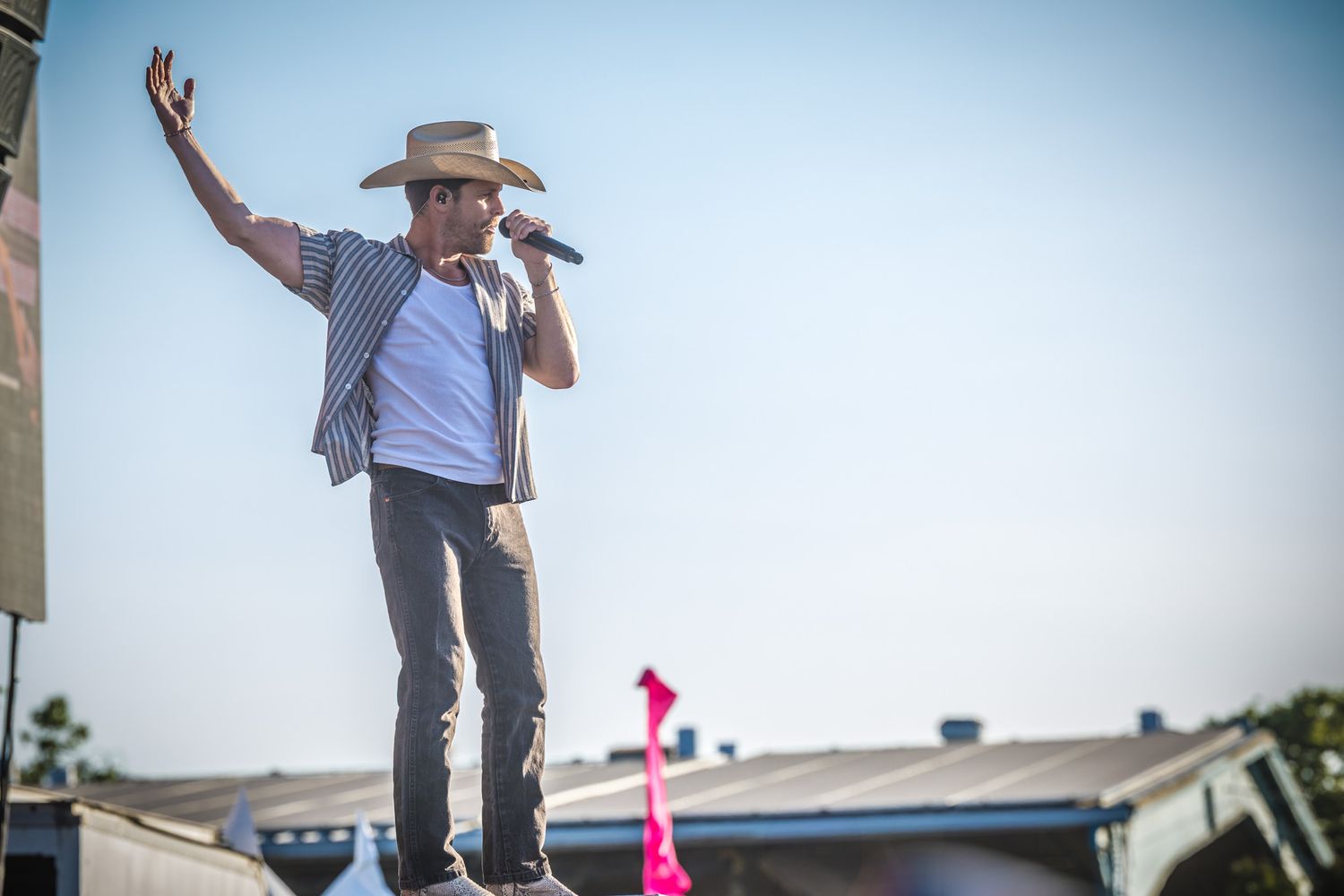 Performer in cowboy hat singing on stage at an outdoor daytime event.