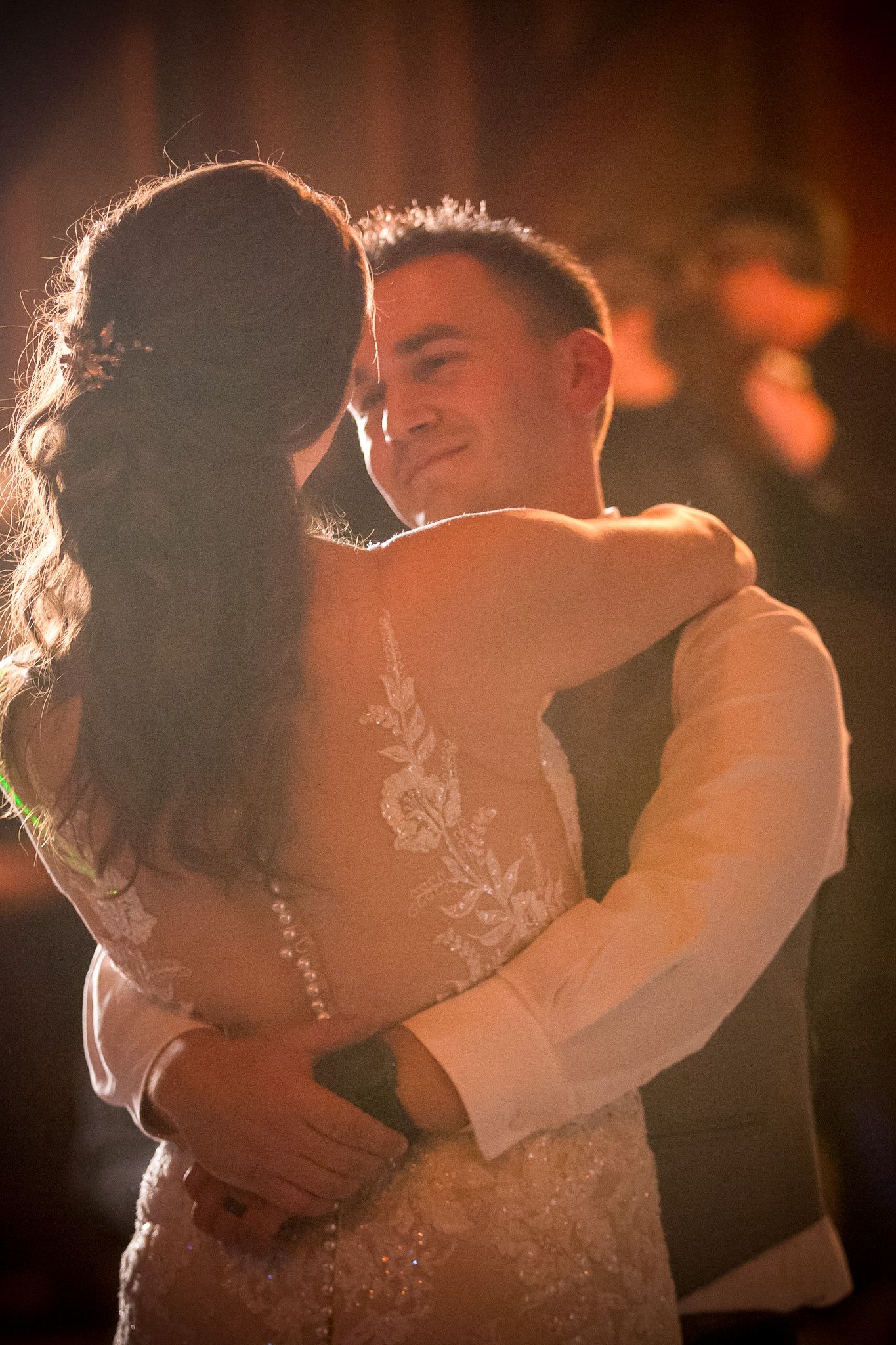 Intimate moment between couple during wedding dance with backlit glow.