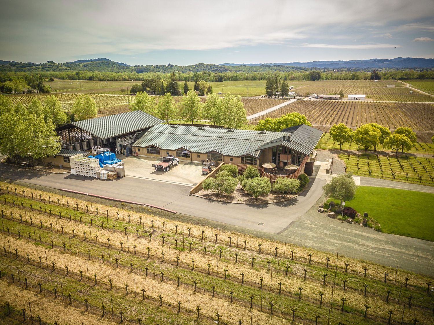 Aerial view of a rustic winery facility with surrounding vineyards and mountain backdrop.