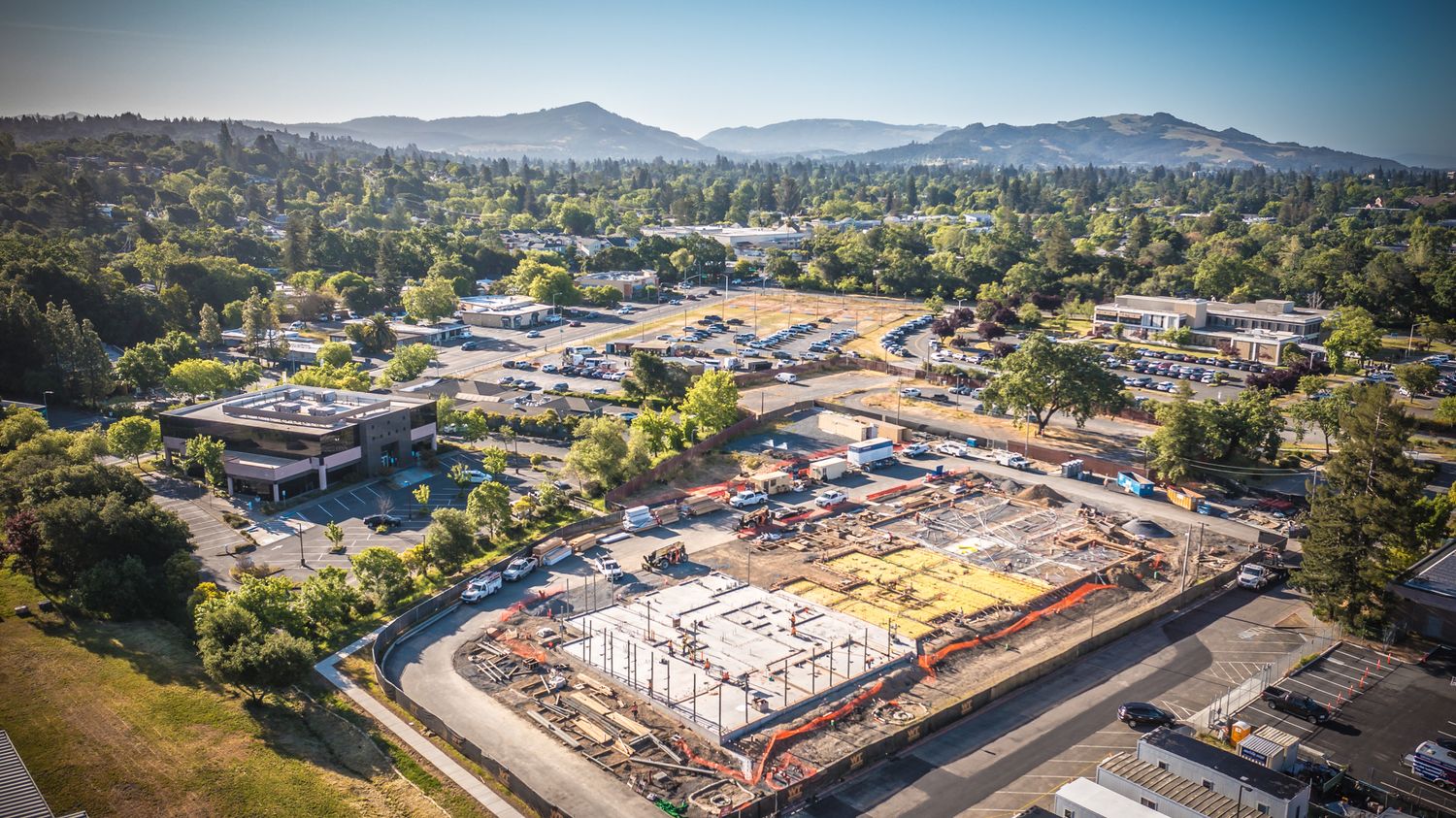Aerial view of a construction site surrounded by buildings and mountains in a suburban area.