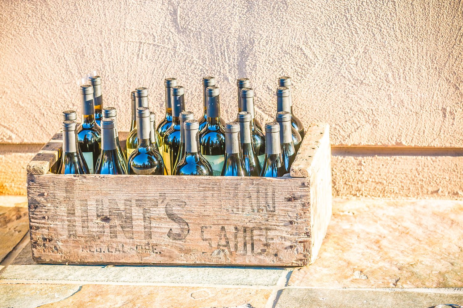 Vintage wooden crate filled with blue wine bottles on stone surface.