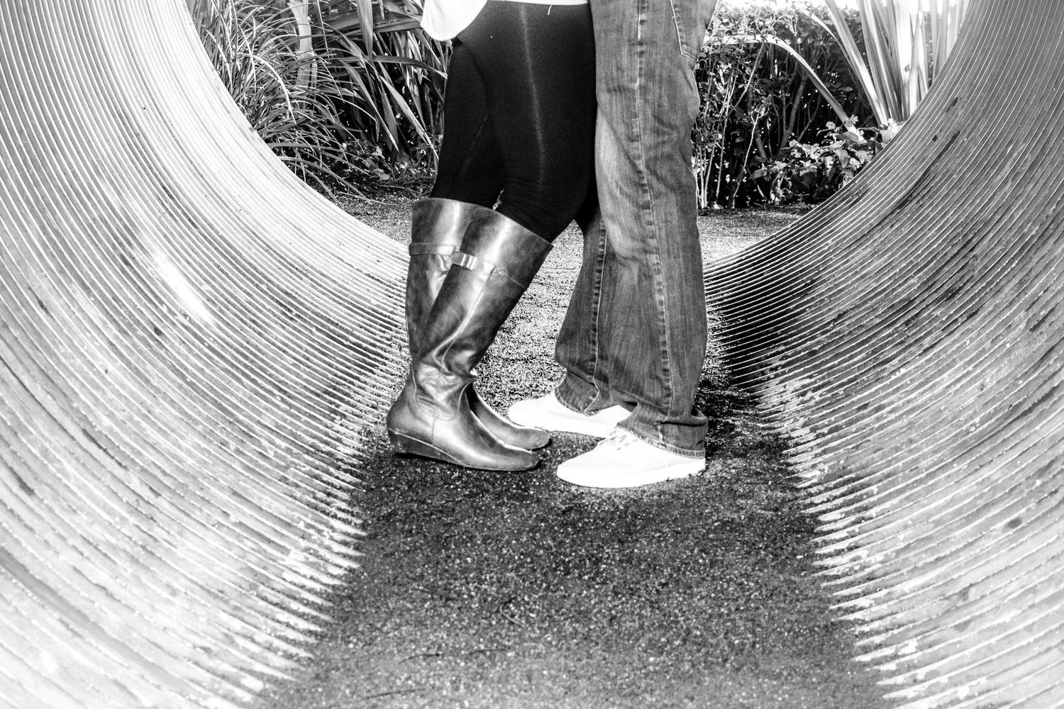 Black and white view of someone wearing contrasting sneakers standing inside a curved concrete drainage pipe.