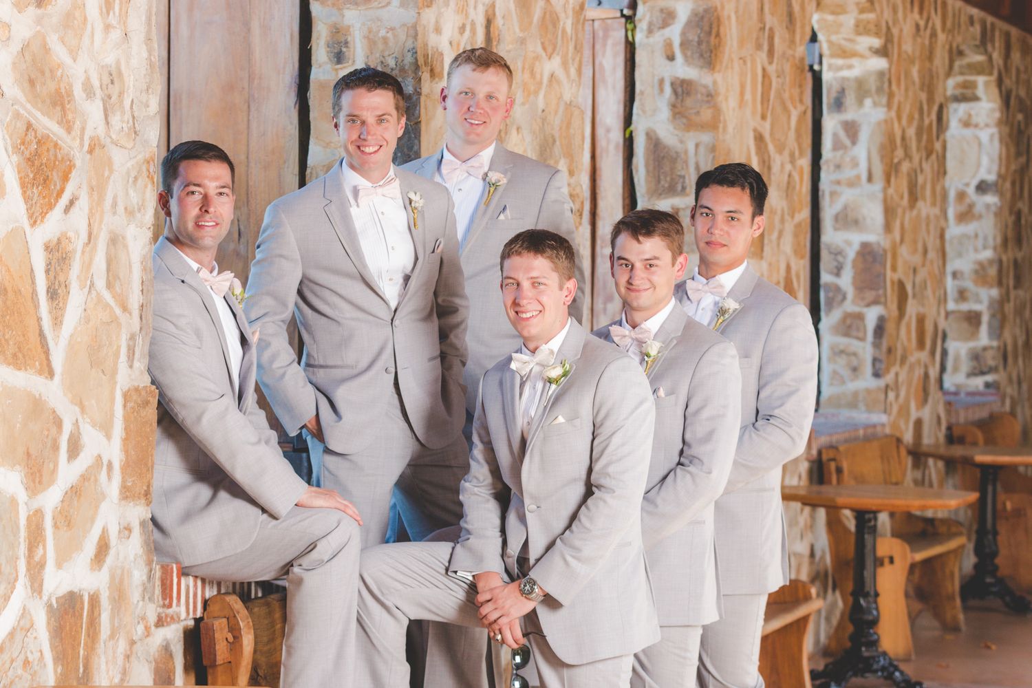 Wedding party in matching light gray suits posed against a stone wall backdrop.