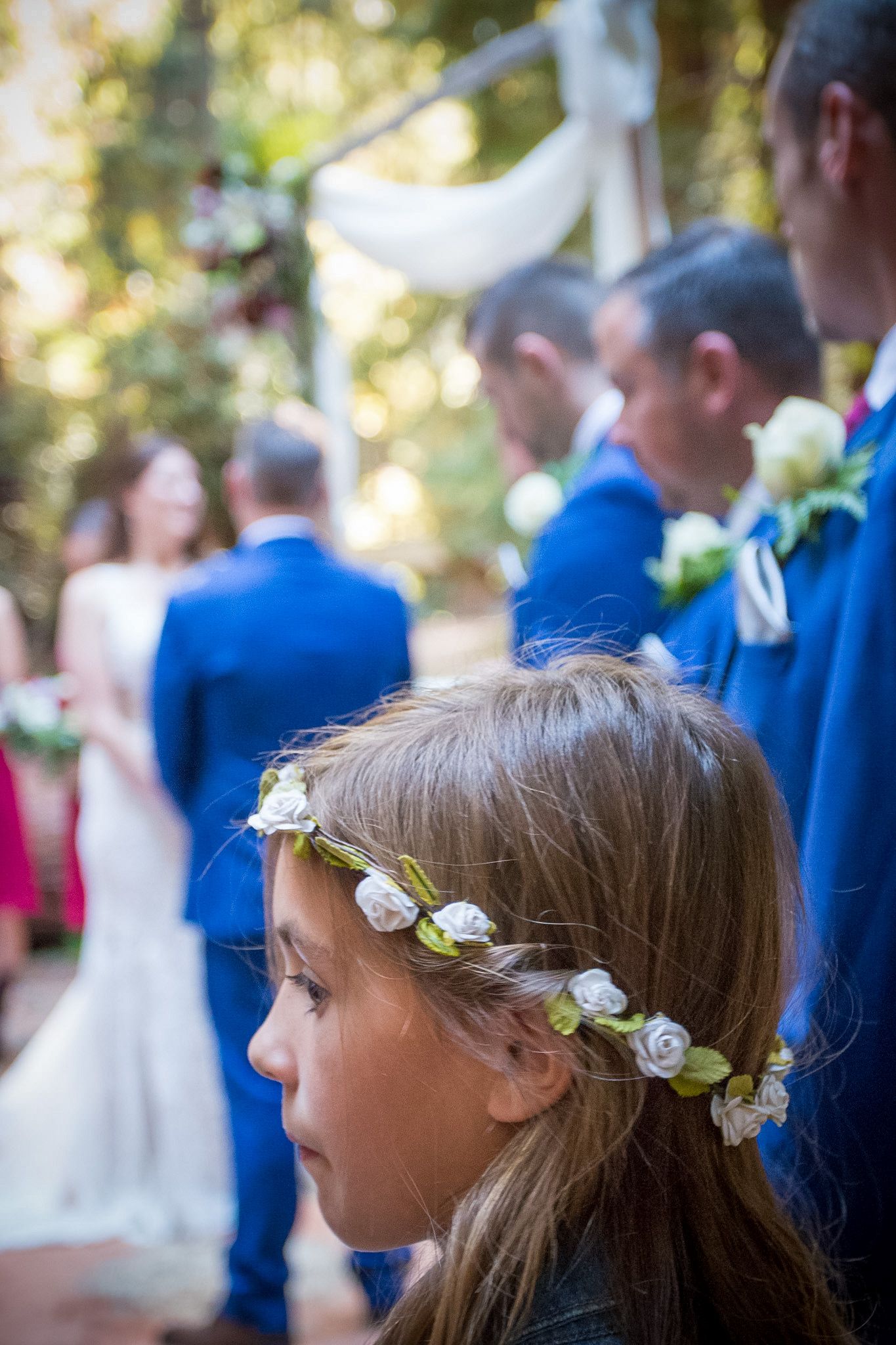 Young flower girl with delicate white floral crown watching wedding ceremony.
