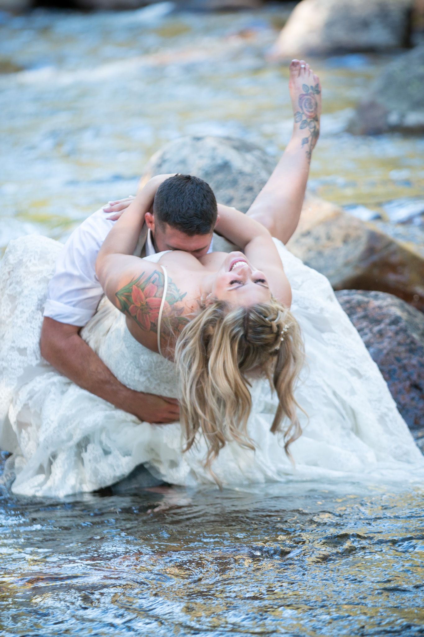 Romantic wedding photo of couple lying on rocks by flowing stream.