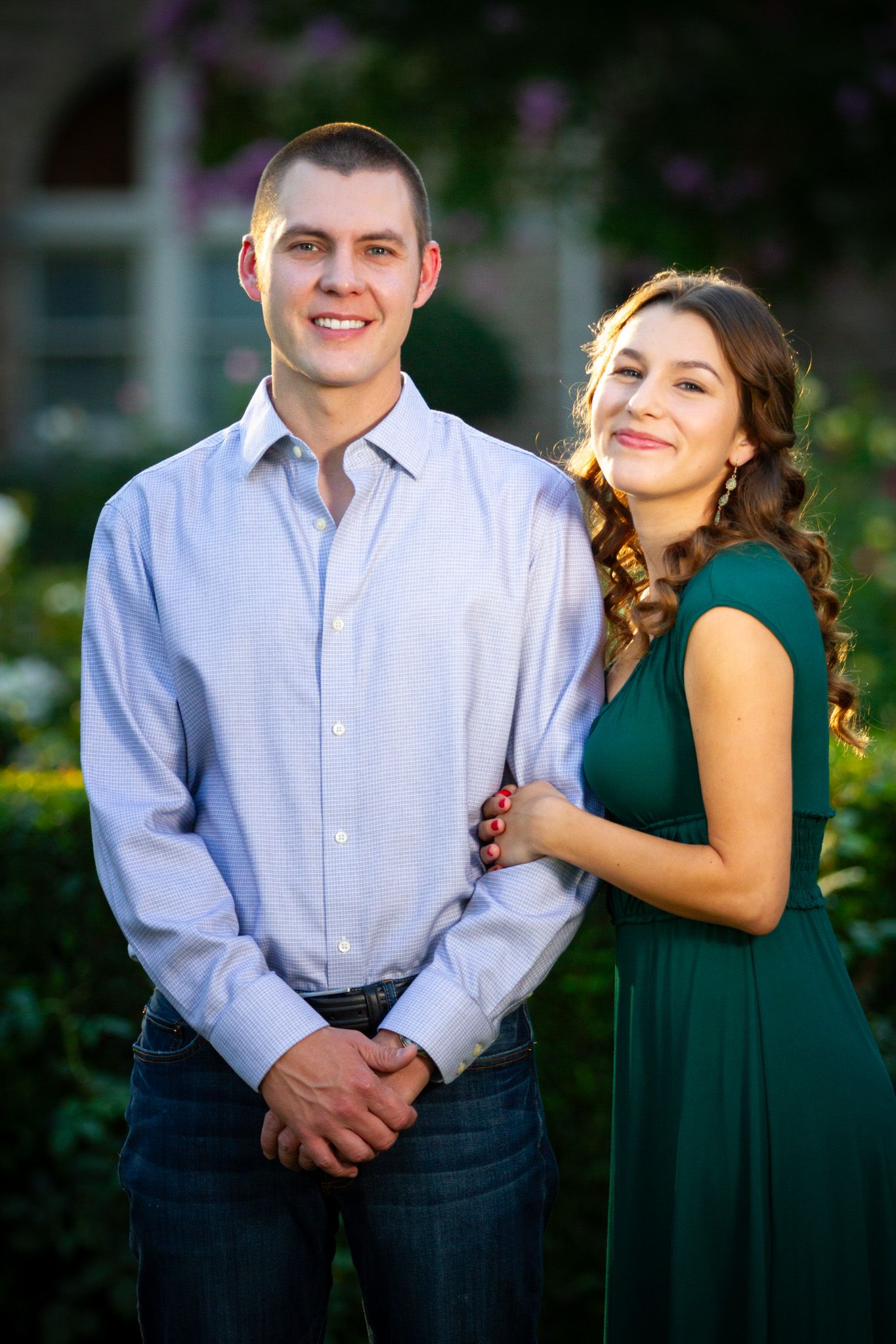 Couple posing outdoors, woman in green dress and man in light blue shirt for engagement photos.