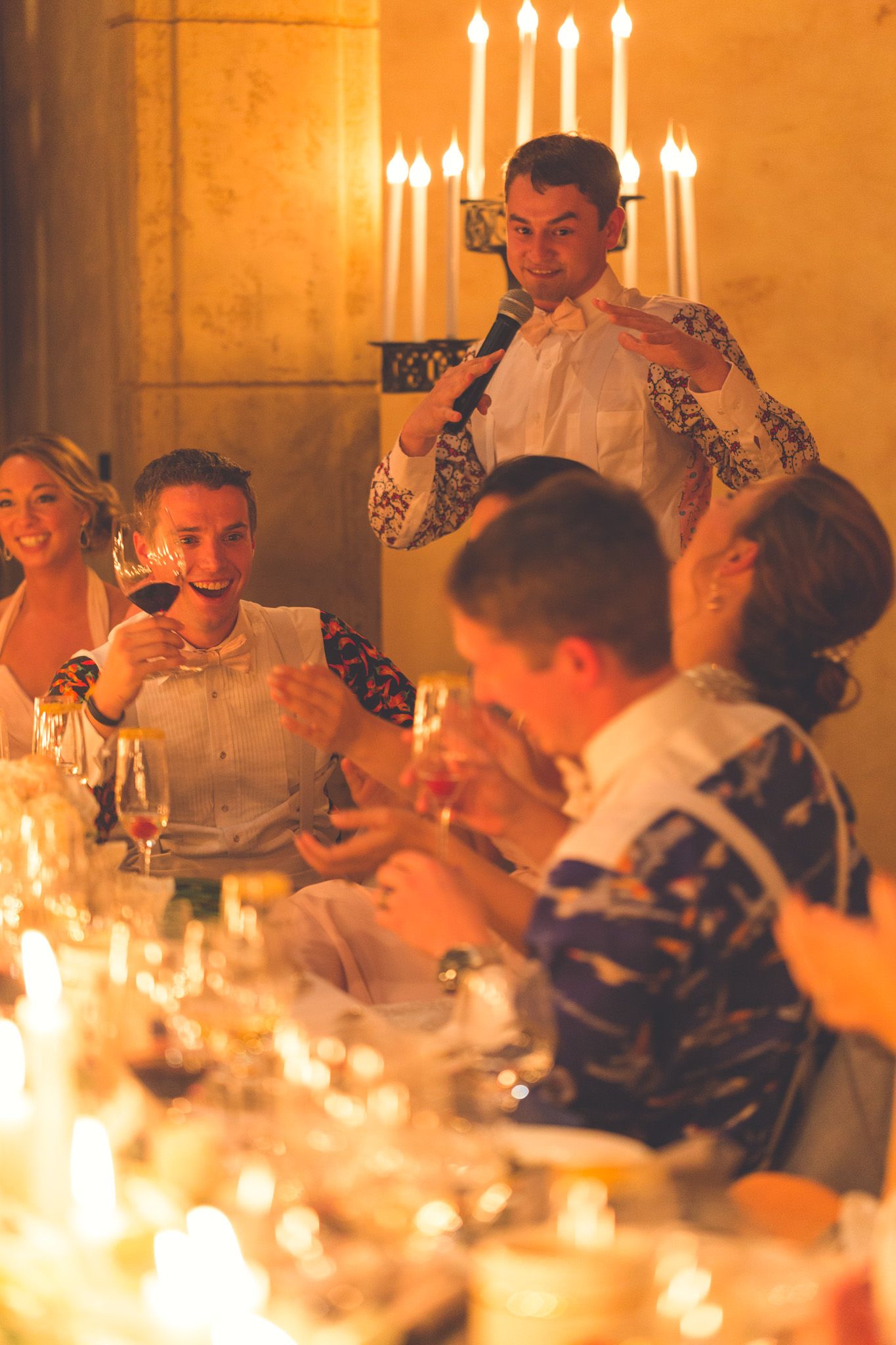 Guests enjoying an elegant candlelit dinner party with wine and glowing ambiance in a warm setting.